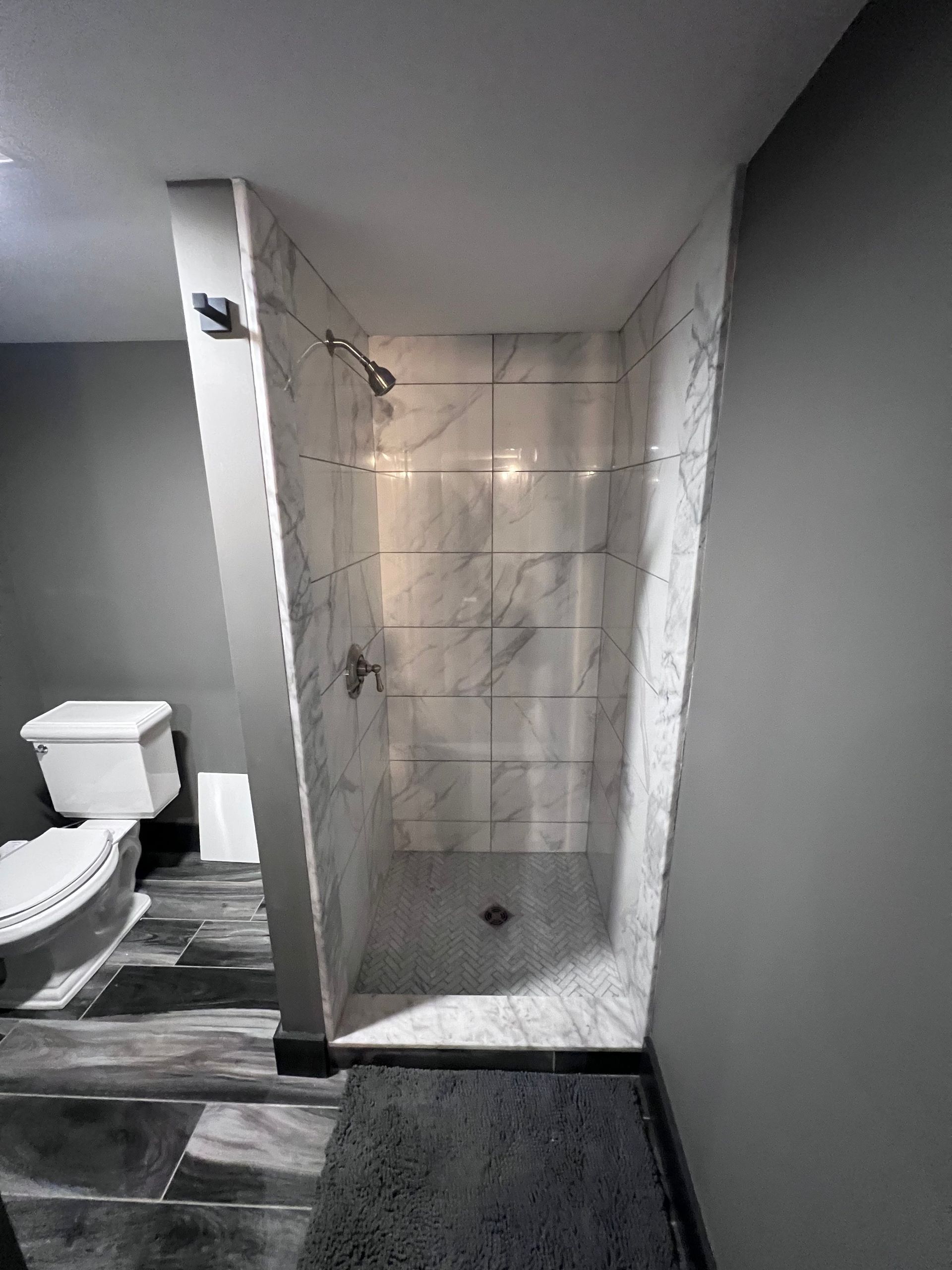 Gray and white marble shower with a toilet on the left.