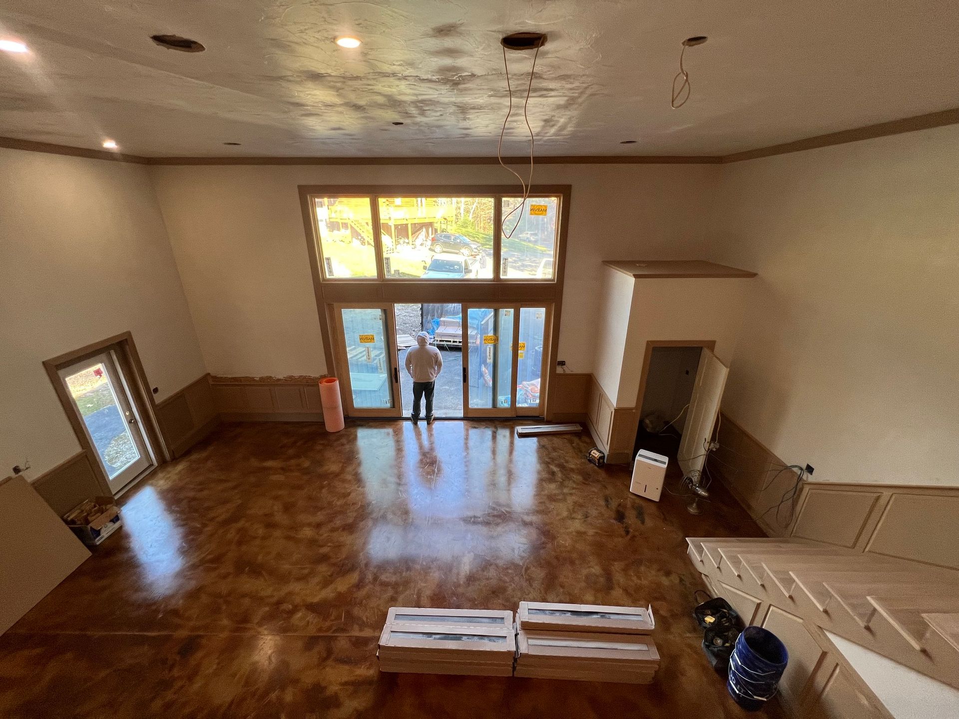 Large room with wood flooring, tall windows, a person in doorway, and construction materials.