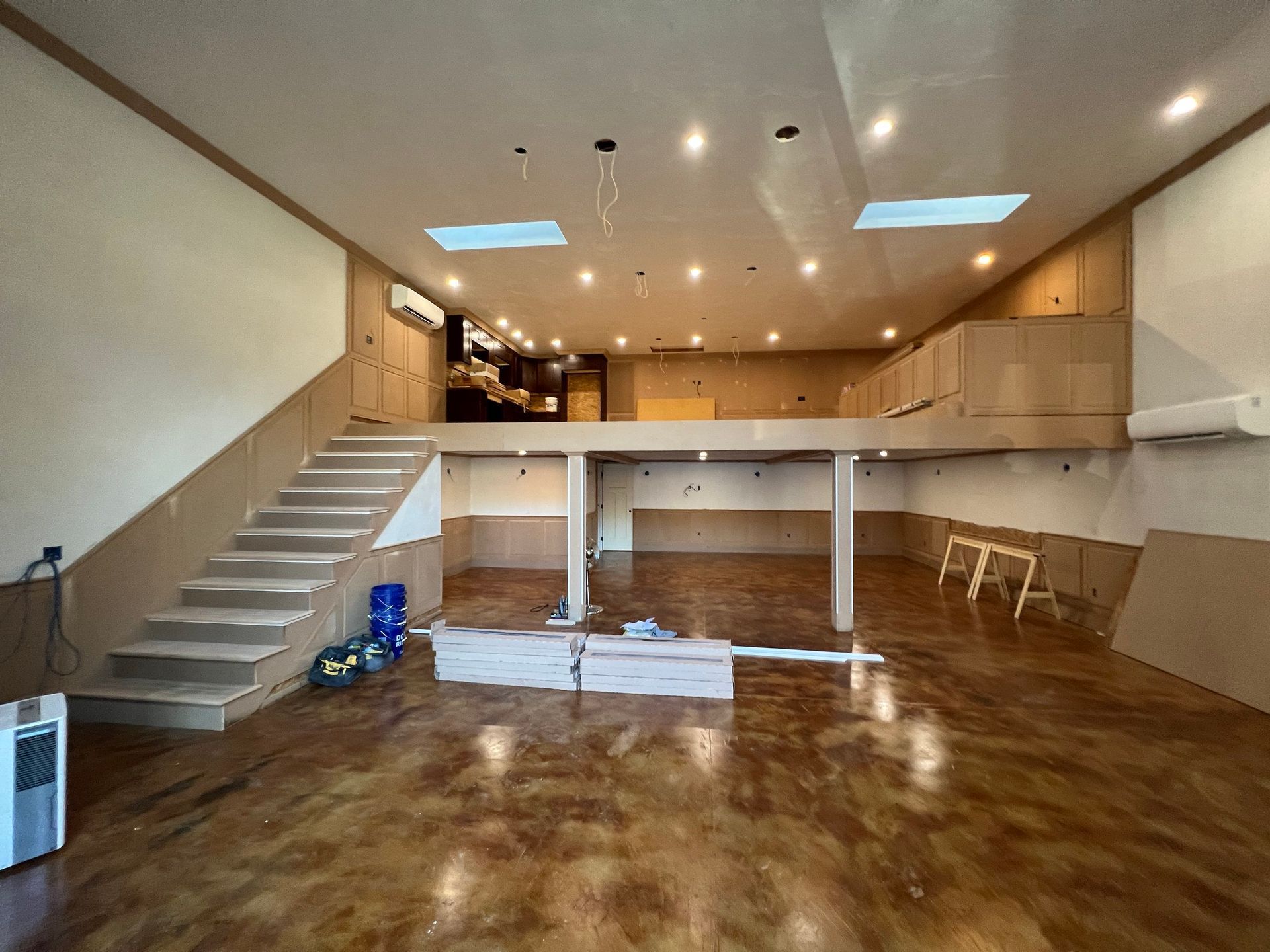 Interior of a large room with a loft and staircase, under construction, with exposed wood and a finished metallic floor.