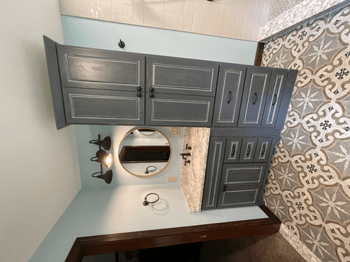 Bathroom with gray cabinets, a round mirror, and patterned floor tiles.