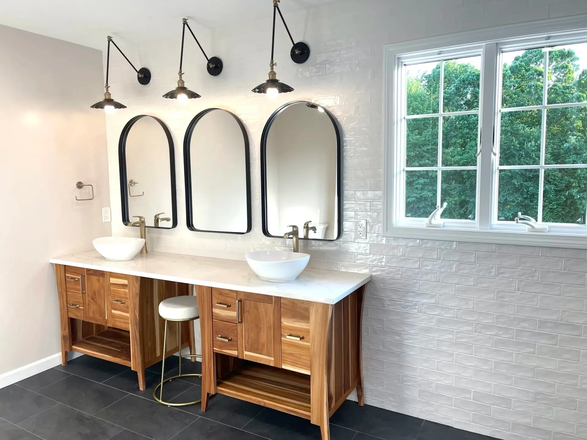 Bathroom with three arch mirrors, white sinks, wooden cabinets, and wall-mounted lights.