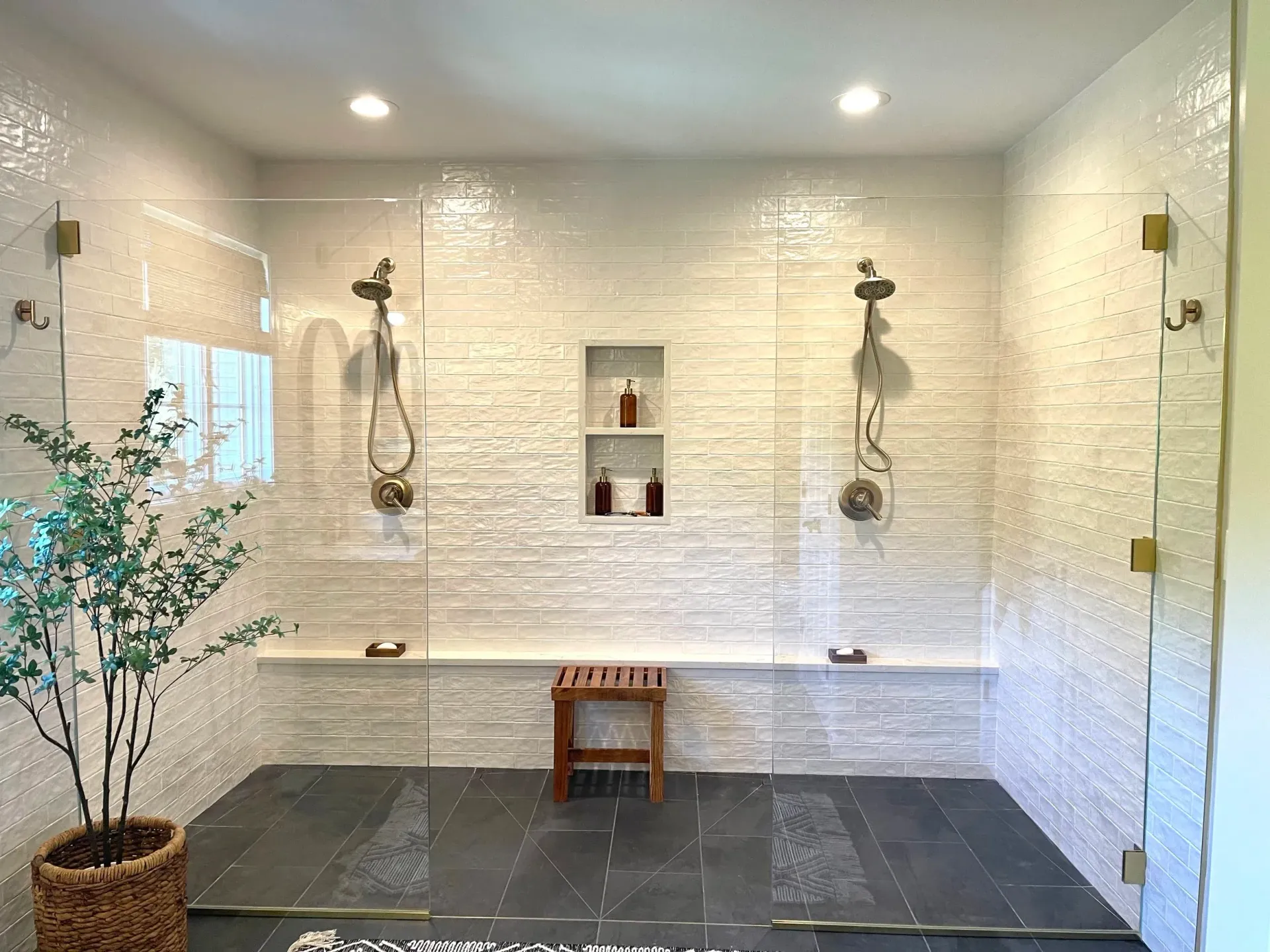 Spacious bathroom with glass showers, white textured tile, stone floor, built-in benches, and a wooden stool.