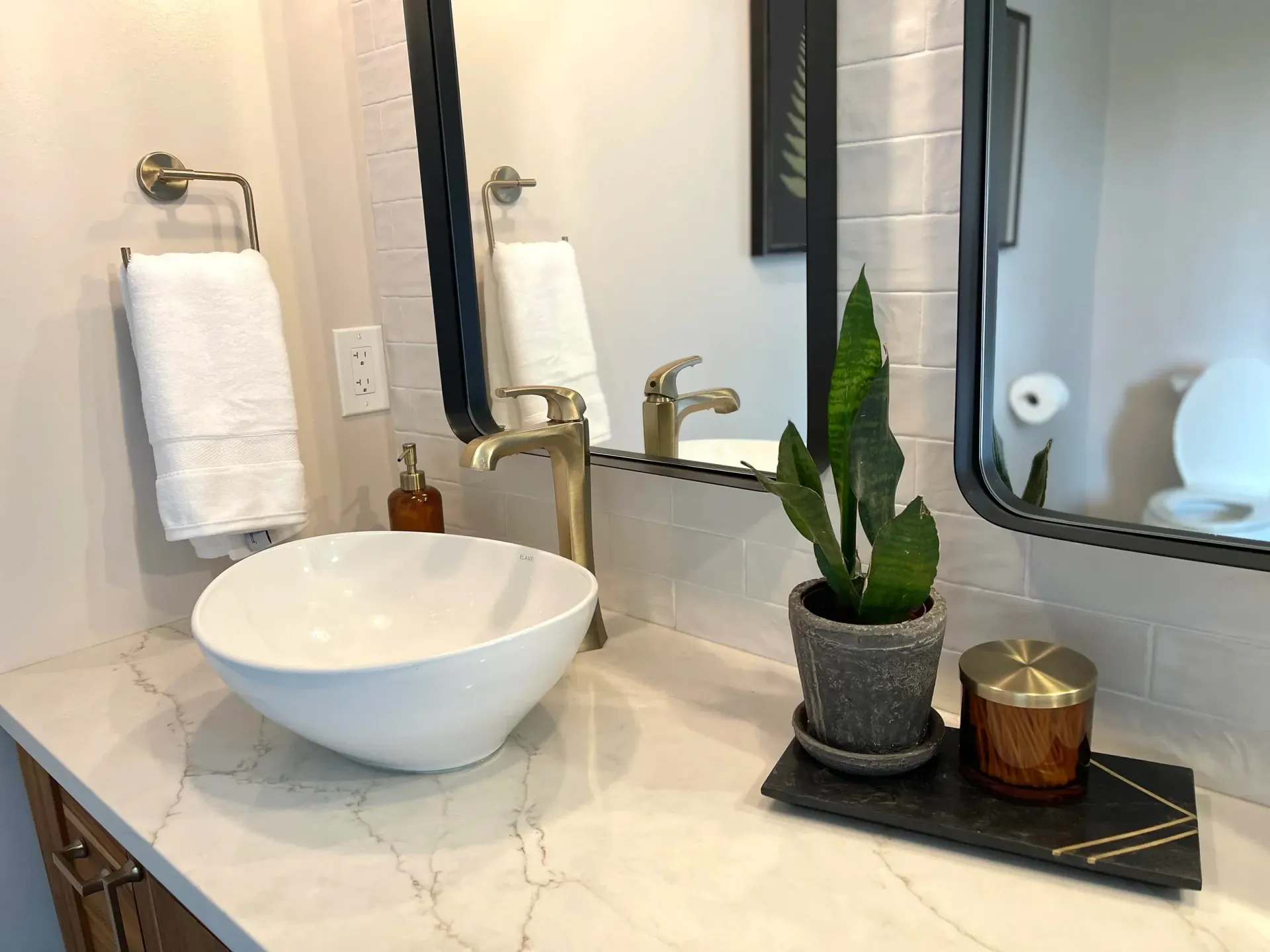 Bathroom vanity with white vessel sink, gold faucet, and potted snake plant.