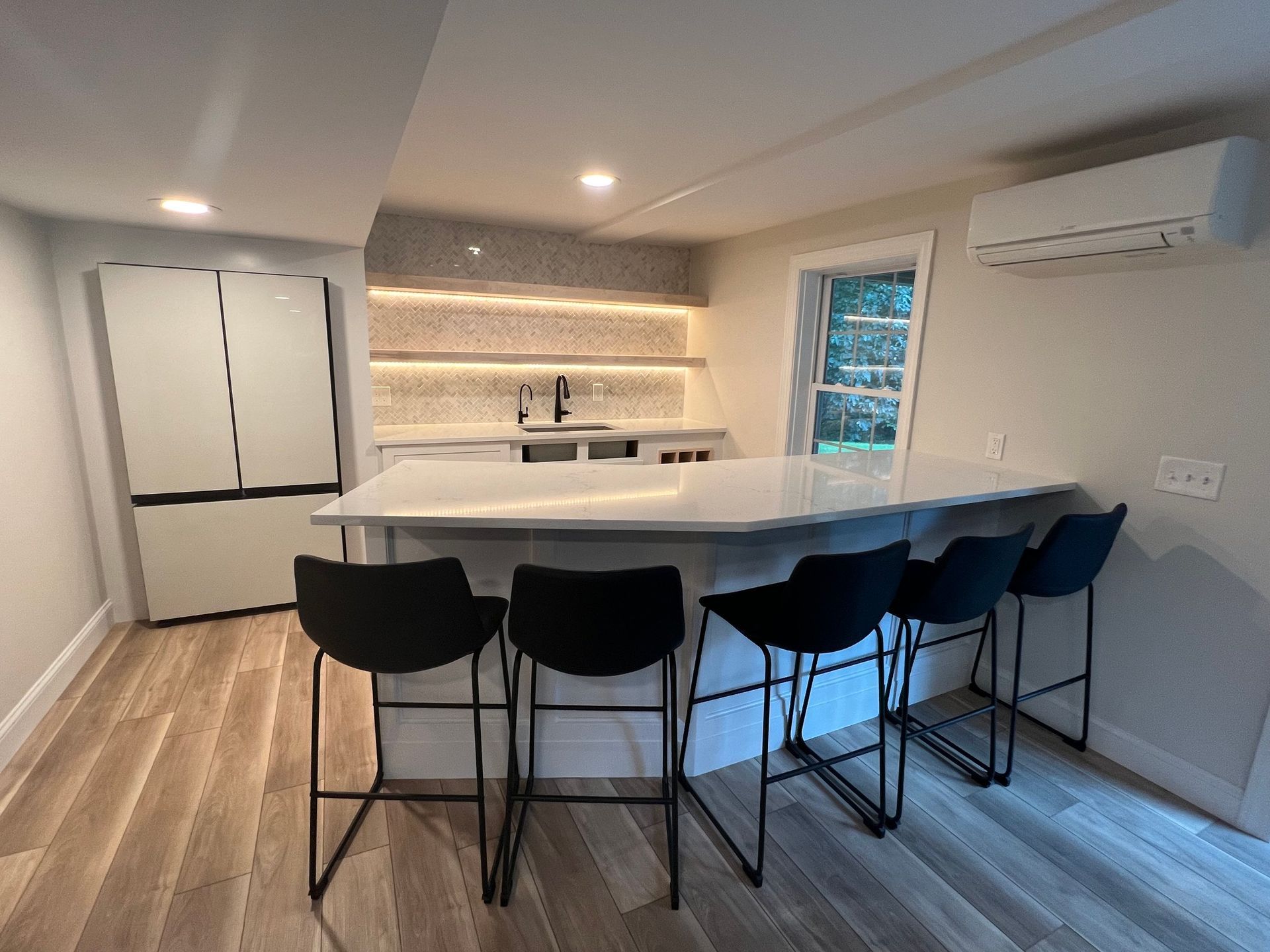 Modern kitchen with island, black stools, and white appliances. White and gray tones.