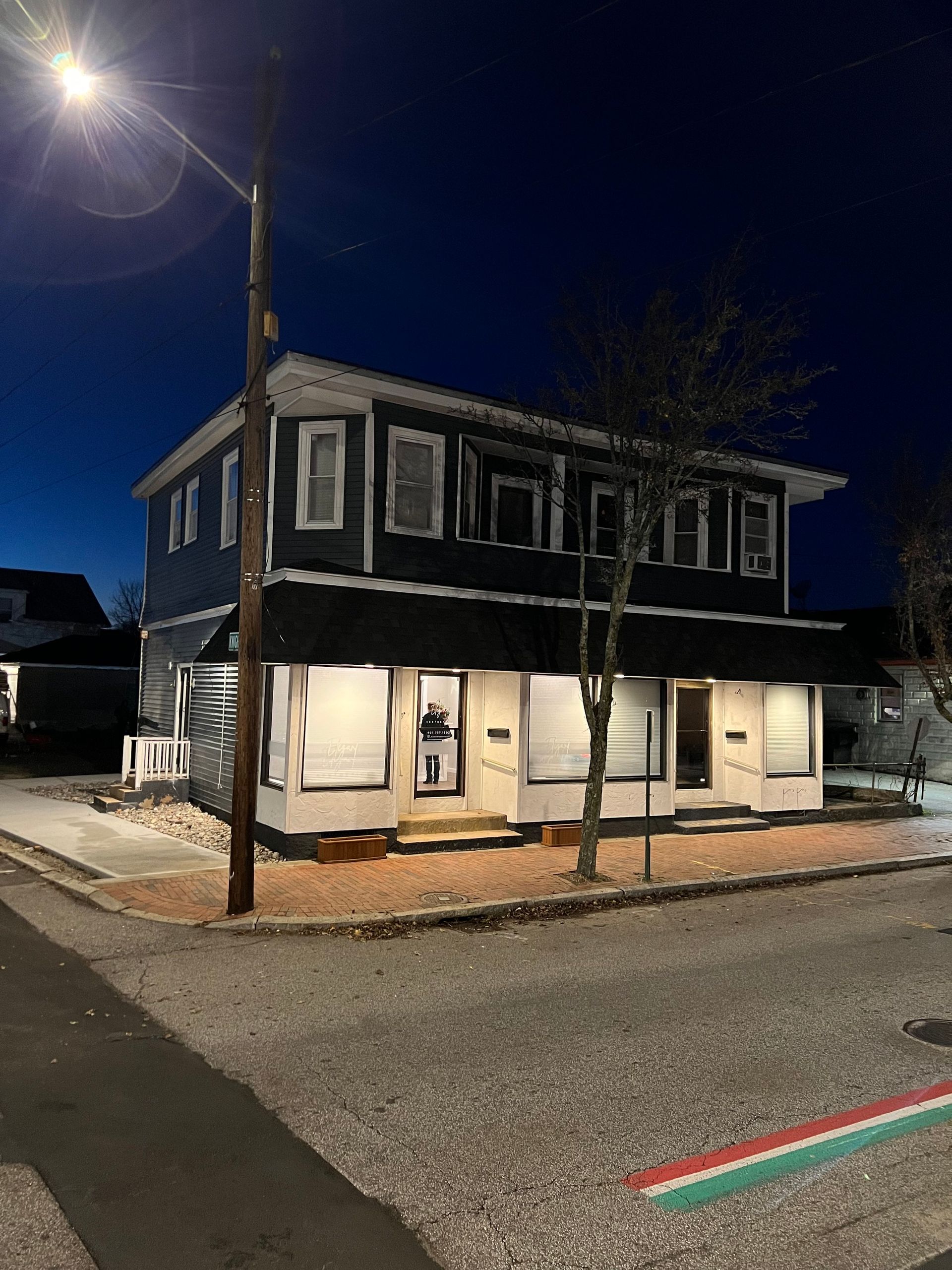 Two-story building at night with lit windows, street corner view, dark blue exterior, white trim, street light.