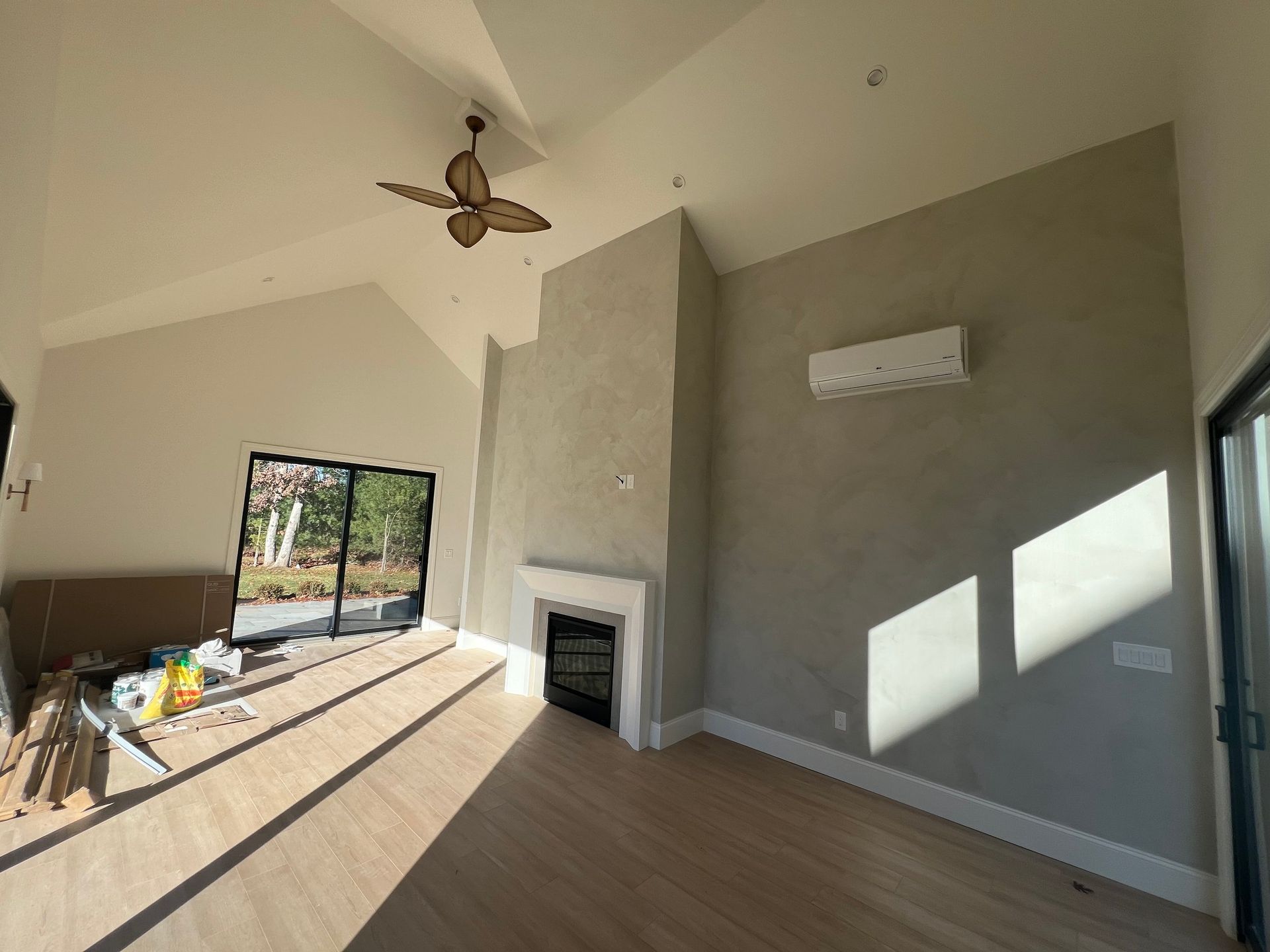 Empty room with light wood floors, high ceiling, fireplace, and sliding glass door.