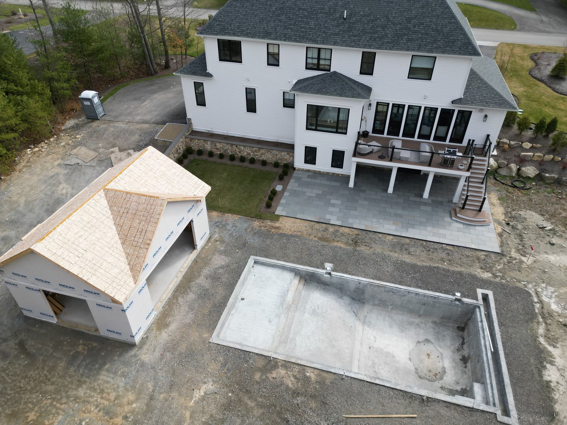 Aerial view of a white house with a partially built garage, a concrete pool, and a back patio.