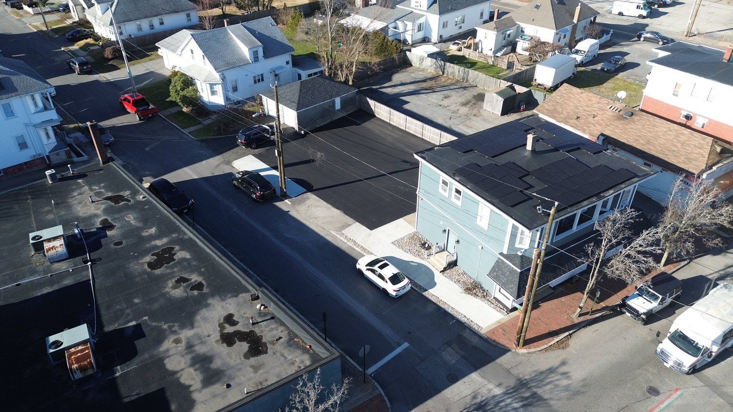 Aerial view of a street with cars, houses, and businesses. Black asphalt road with parked and moving vehicles.