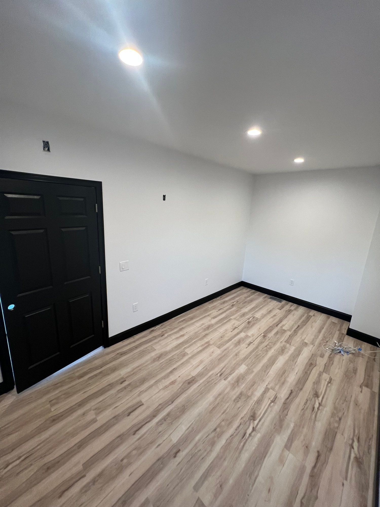 Empty room with light wood flooring, white walls, black door and trim, recessed lighting.