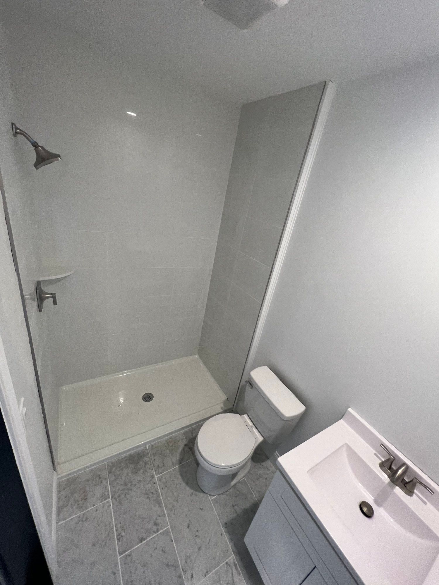 Modern bathroom with a shower, toilet, and sink. Gray tile floor and walls.