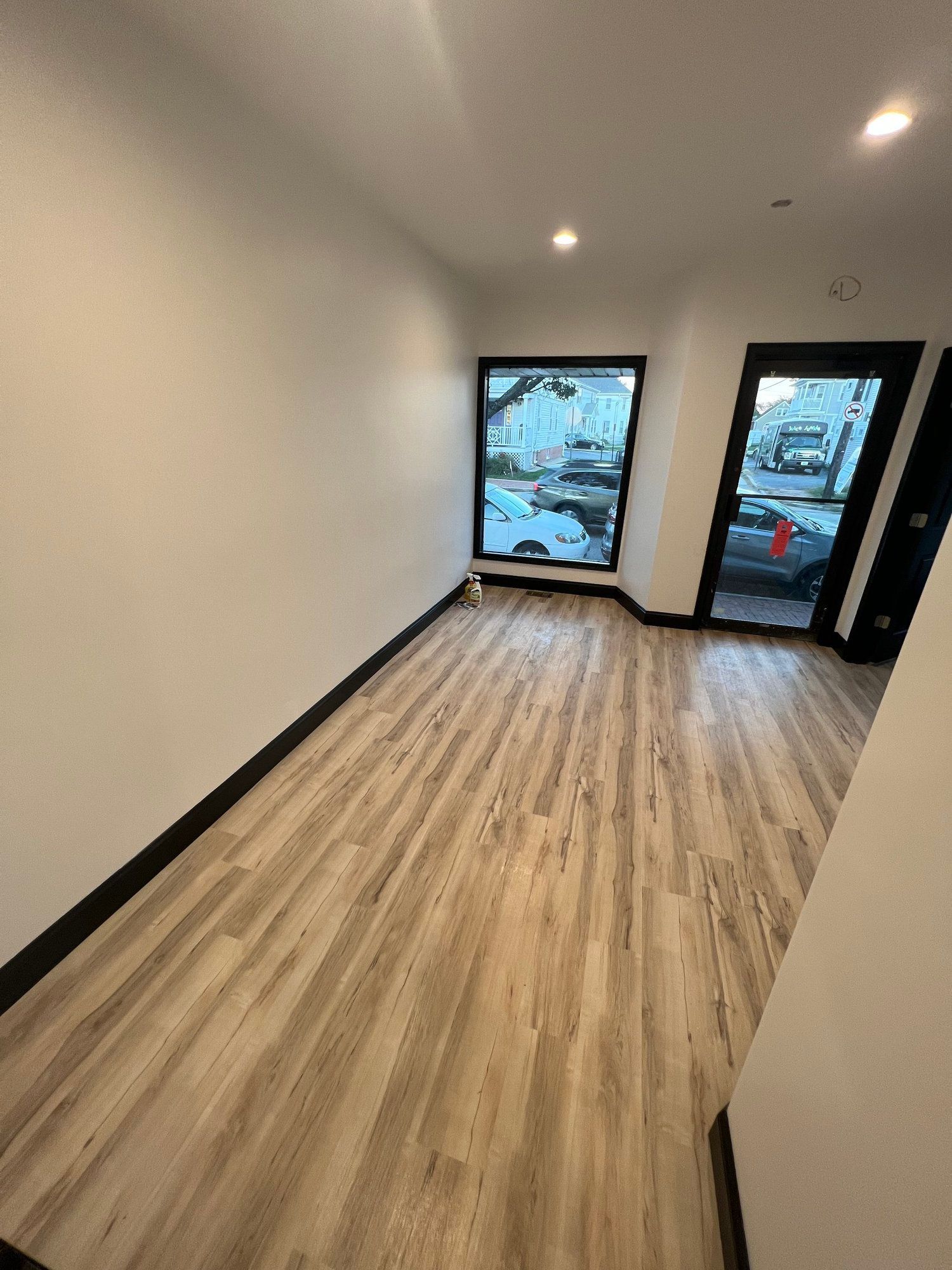 Empty room with light wood-look flooring, white walls, black trim, windows, and a doorway.