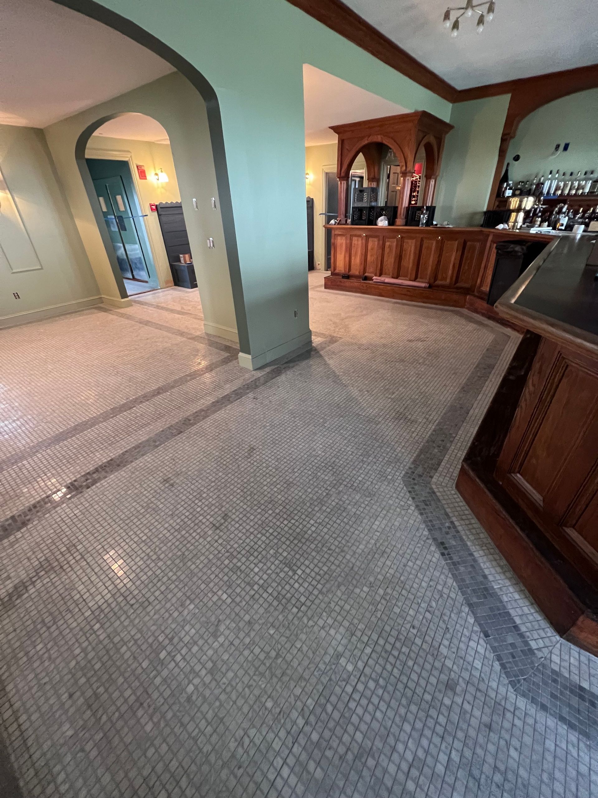 Interior shot of a bar with mosaic tile floors and a wooden bar, green walls, and archways.