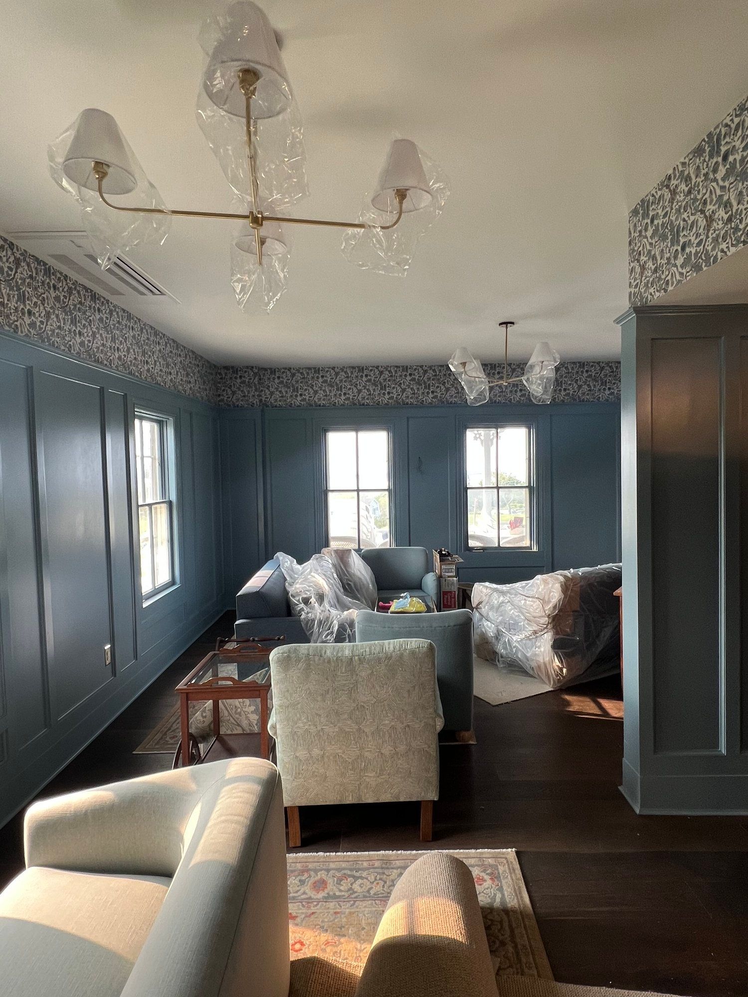 Living room with blue walls, two chandeliers, and furniture covered in plastic.