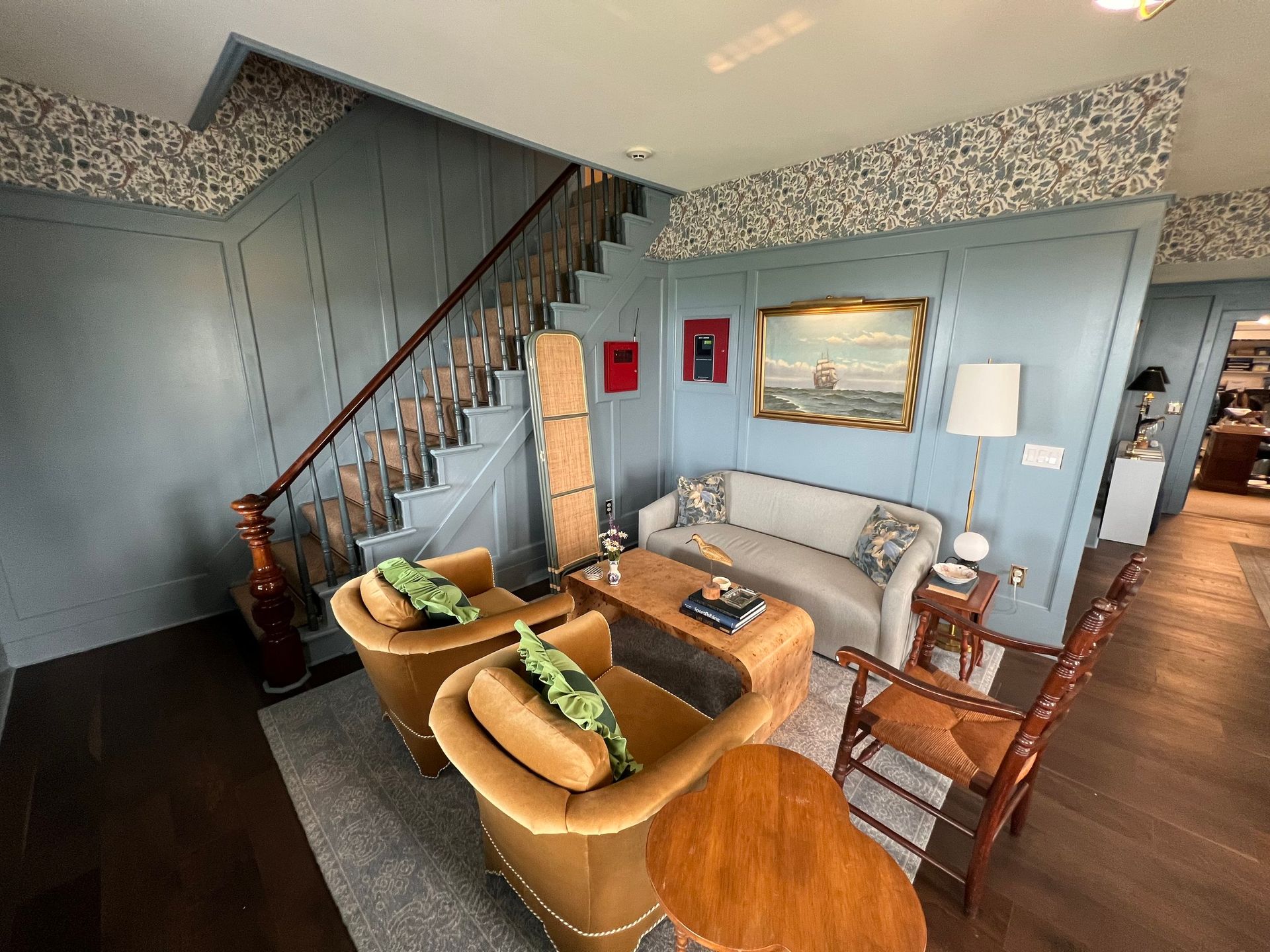 Living room with staircase and seating in shades of blue and gold; wood floors.