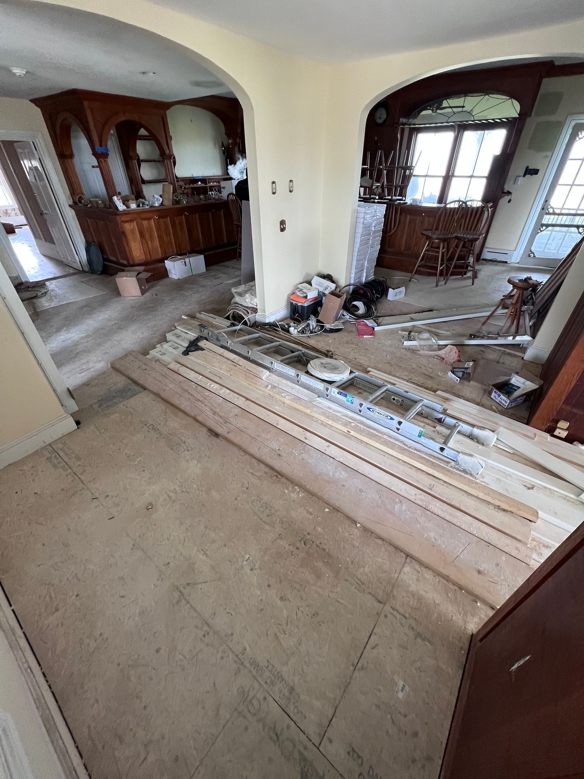 Renovation in progress: Kitchen with wood cabinets, supplies on floor, archways, and debris.