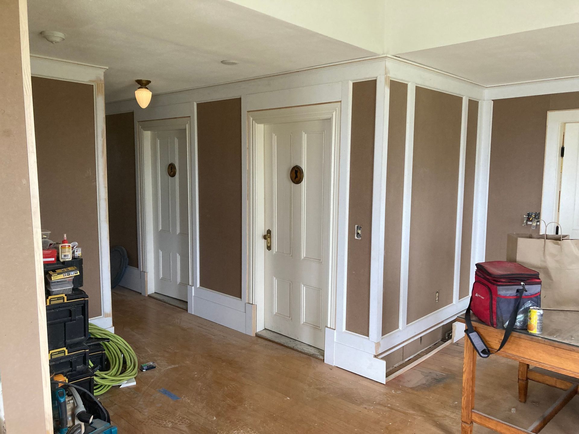 Brown and white hallway with two doors and wooden floor under construction.
