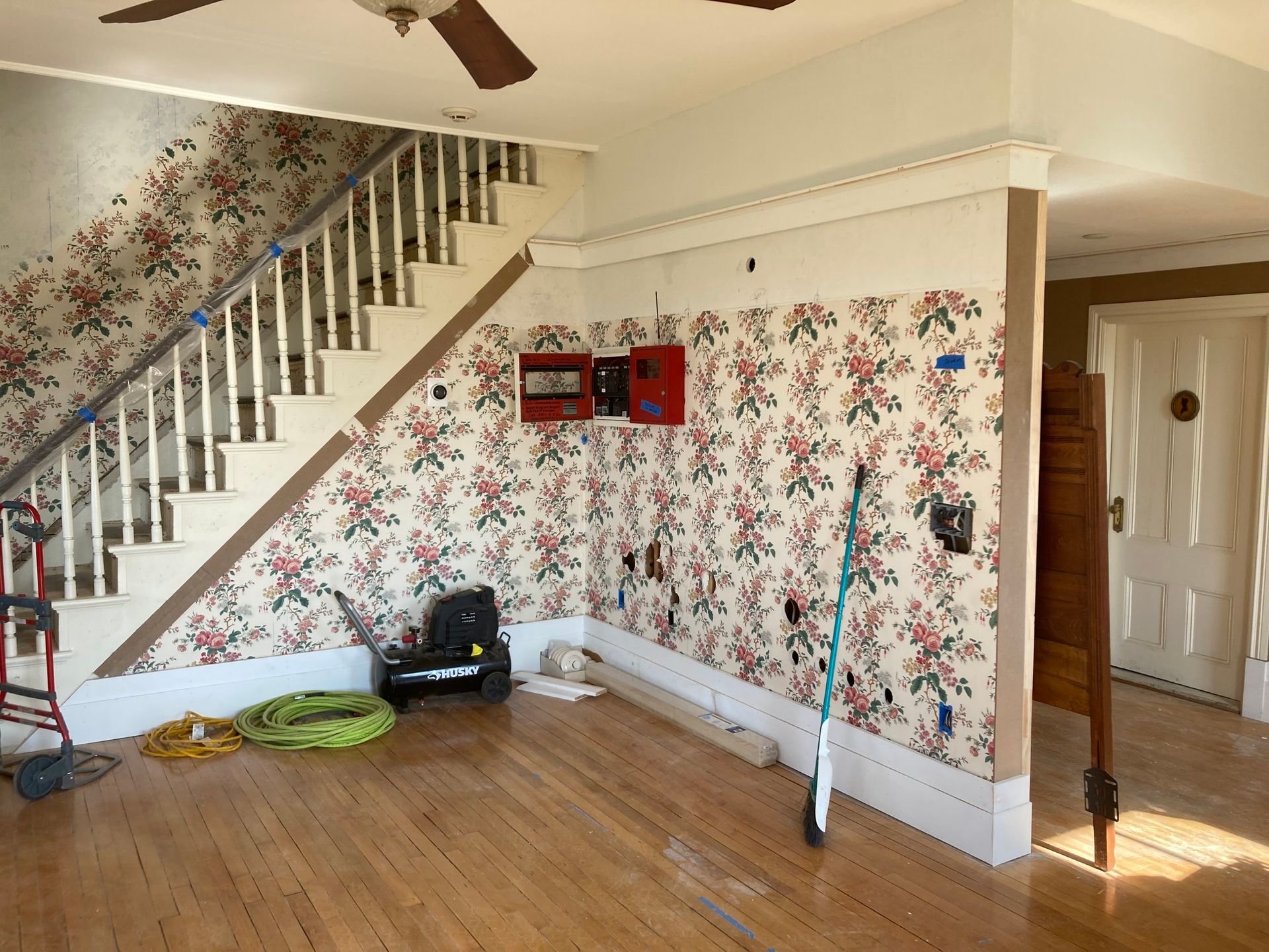 Interior with floral wallpaper, staircase, hardwood floors, and electrical work in progress.