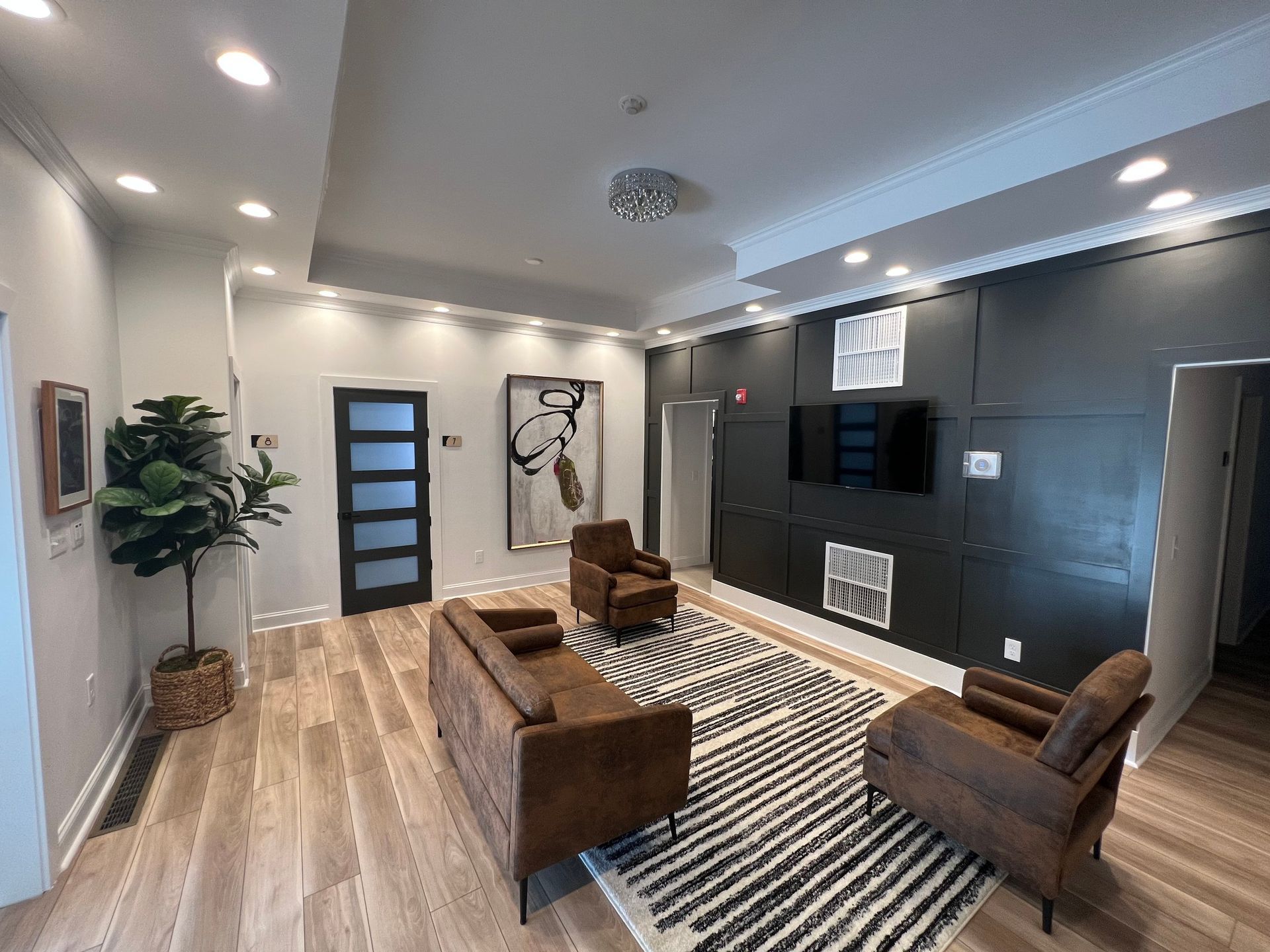 Modern living room with brown leather furniture, black accent wall, rug, and art.