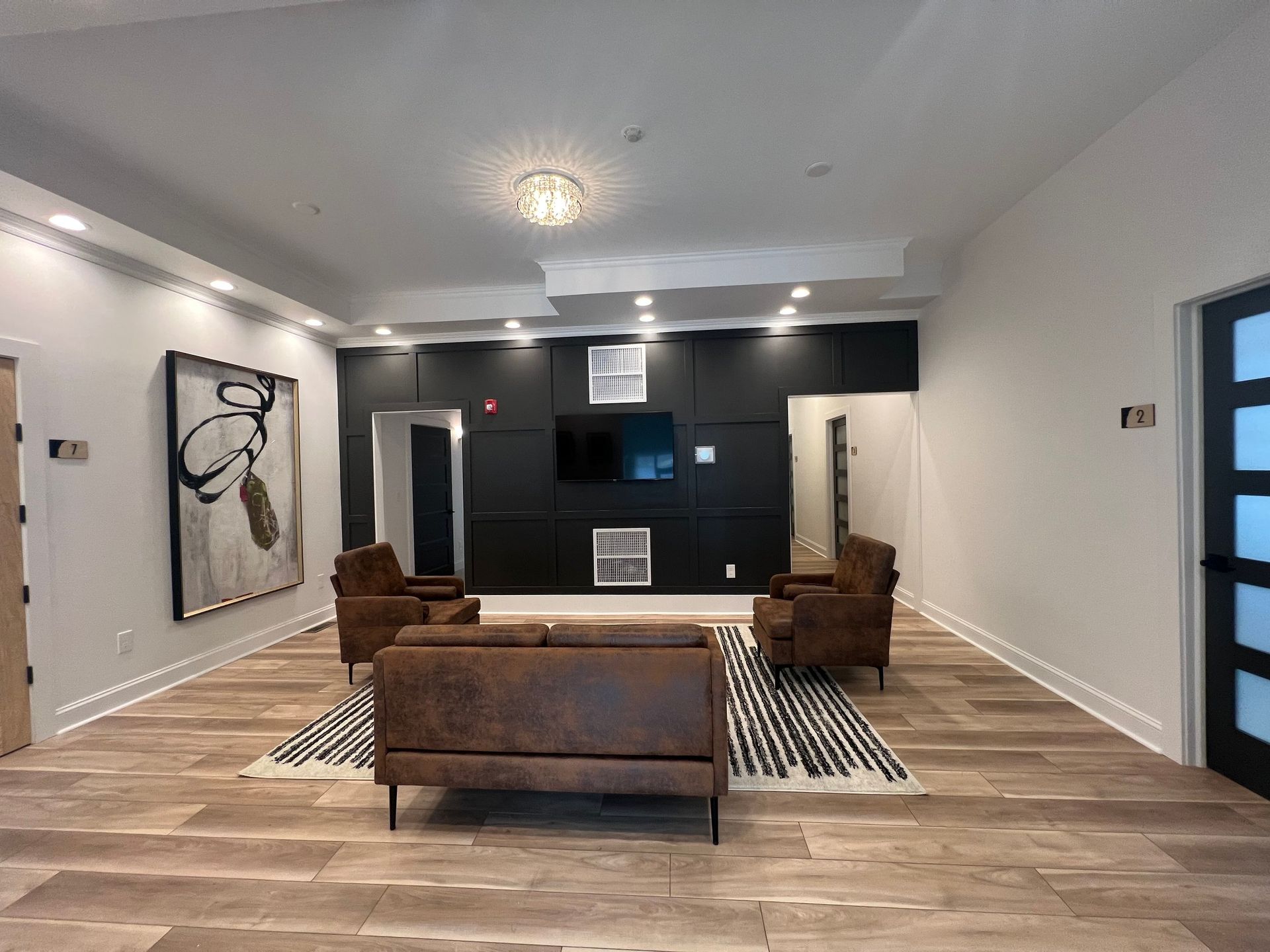 A modern lounge with brown furniture, black accent wall, and wood-look flooring.