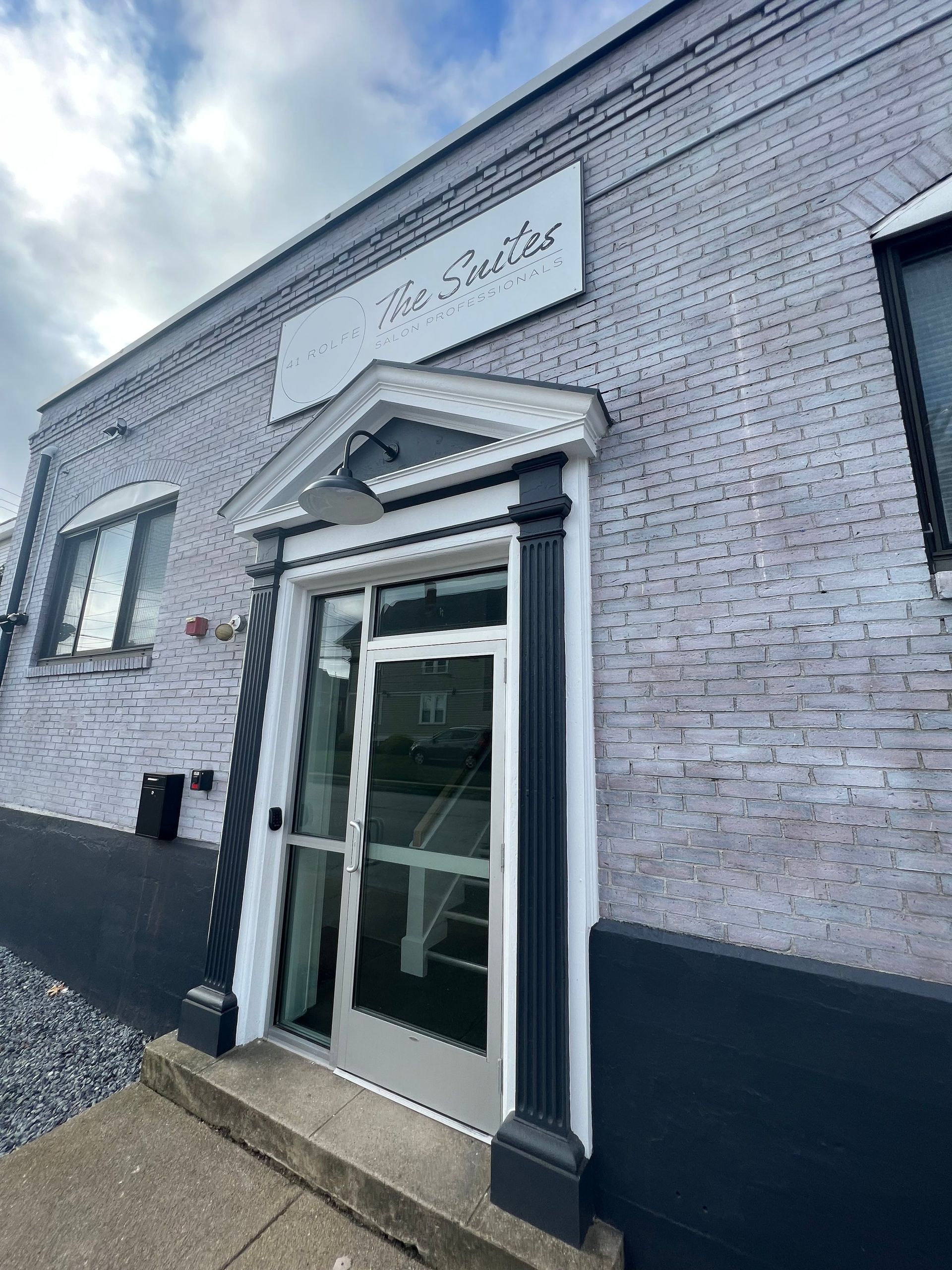 Exterior of The Studio, a white brick building with a black door frame and sign above the door.