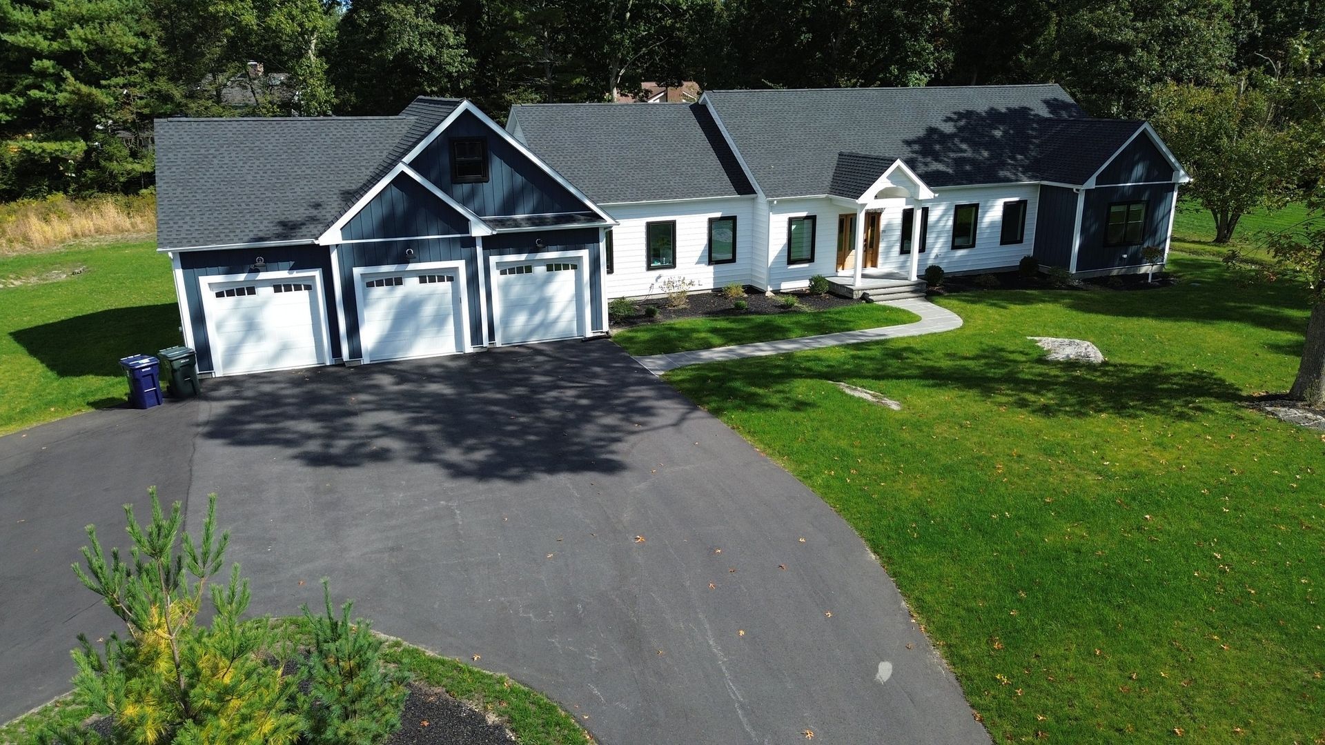 A modern, white and navy blue house with a three-car garage and long black driveway.