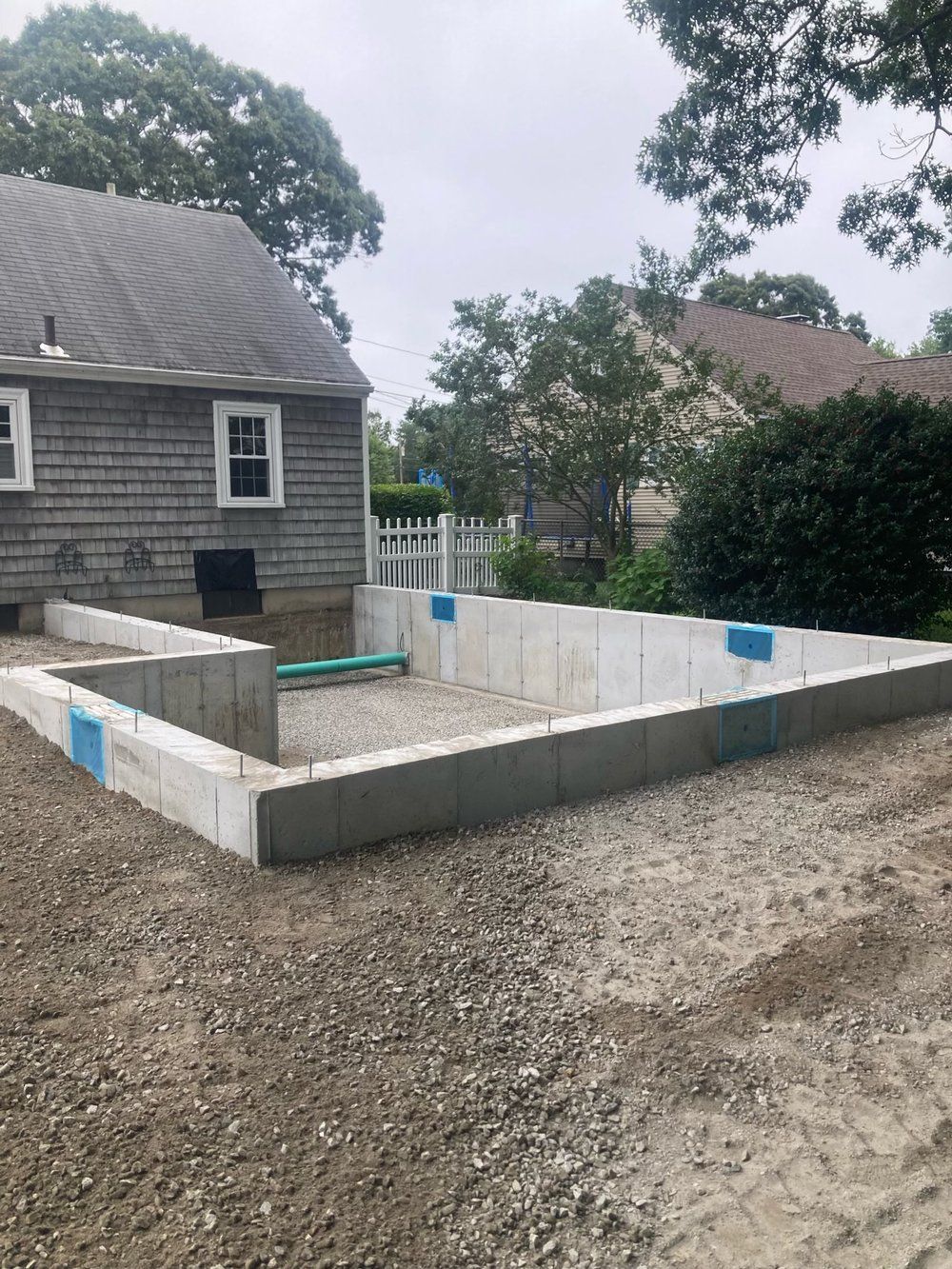 Concrete foundation walls being built next to a house under an overcast sky.