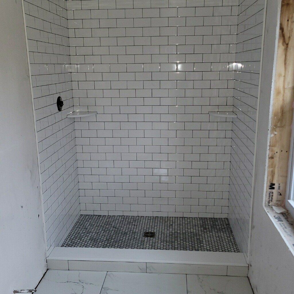 Shower stall with white subway tiles and mosaic floor. Shower is under construction.