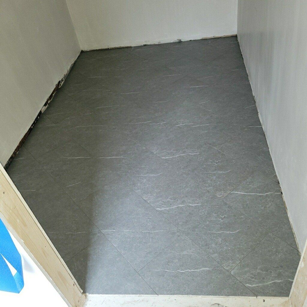 Gray tiled floor in an enclosed space with white walls, possibly under construction.
