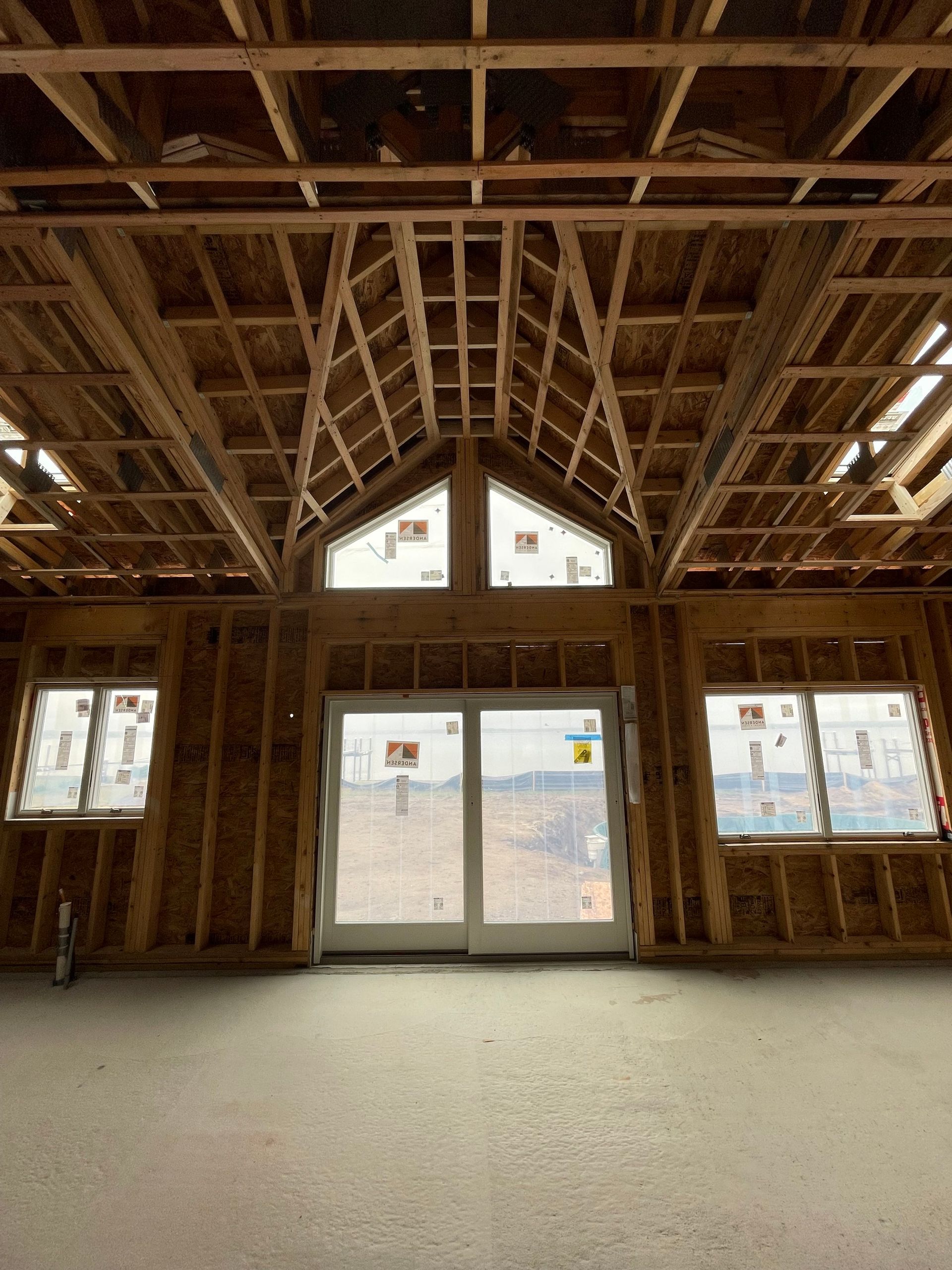 Interior framing of a building under construction, showing wooden beams, windows, and a sliding glass door.