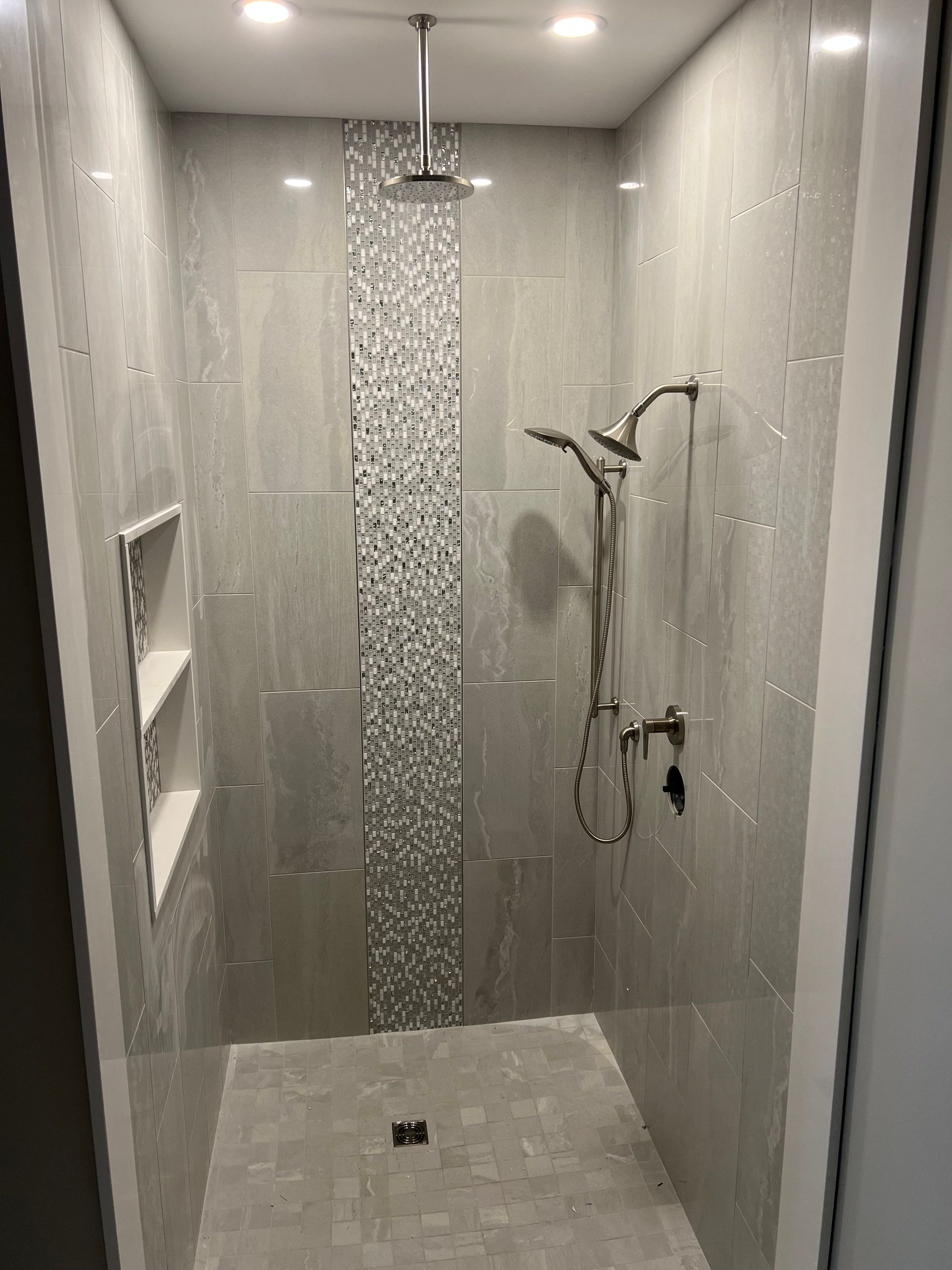 Modern shower with gray tiled walls, recessed shelf, and silver fixtures.