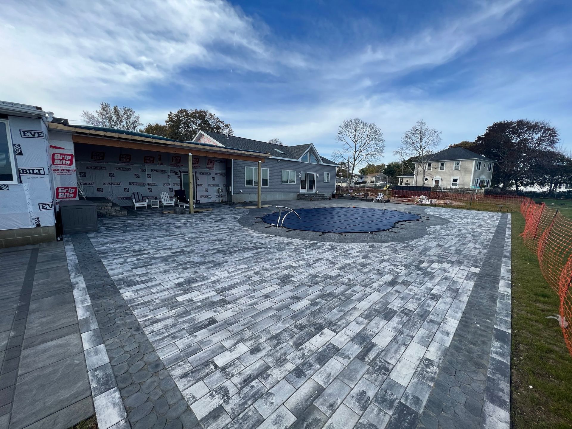Patio with gray pavers, a pool with a cover, and a house under construction on a sunny day.