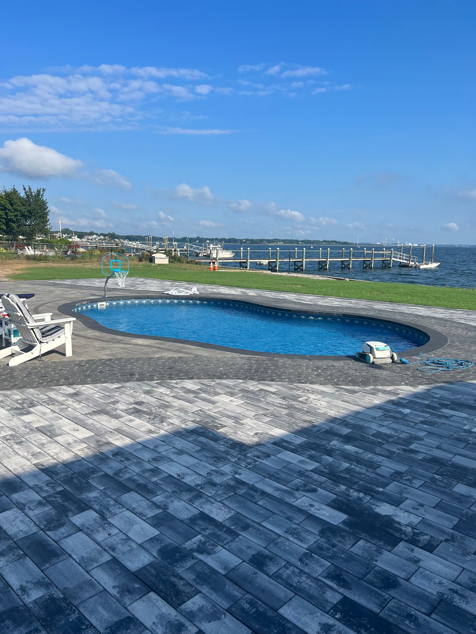 Oval pool near a waterfront with docks and boats under a bright blue sky.
