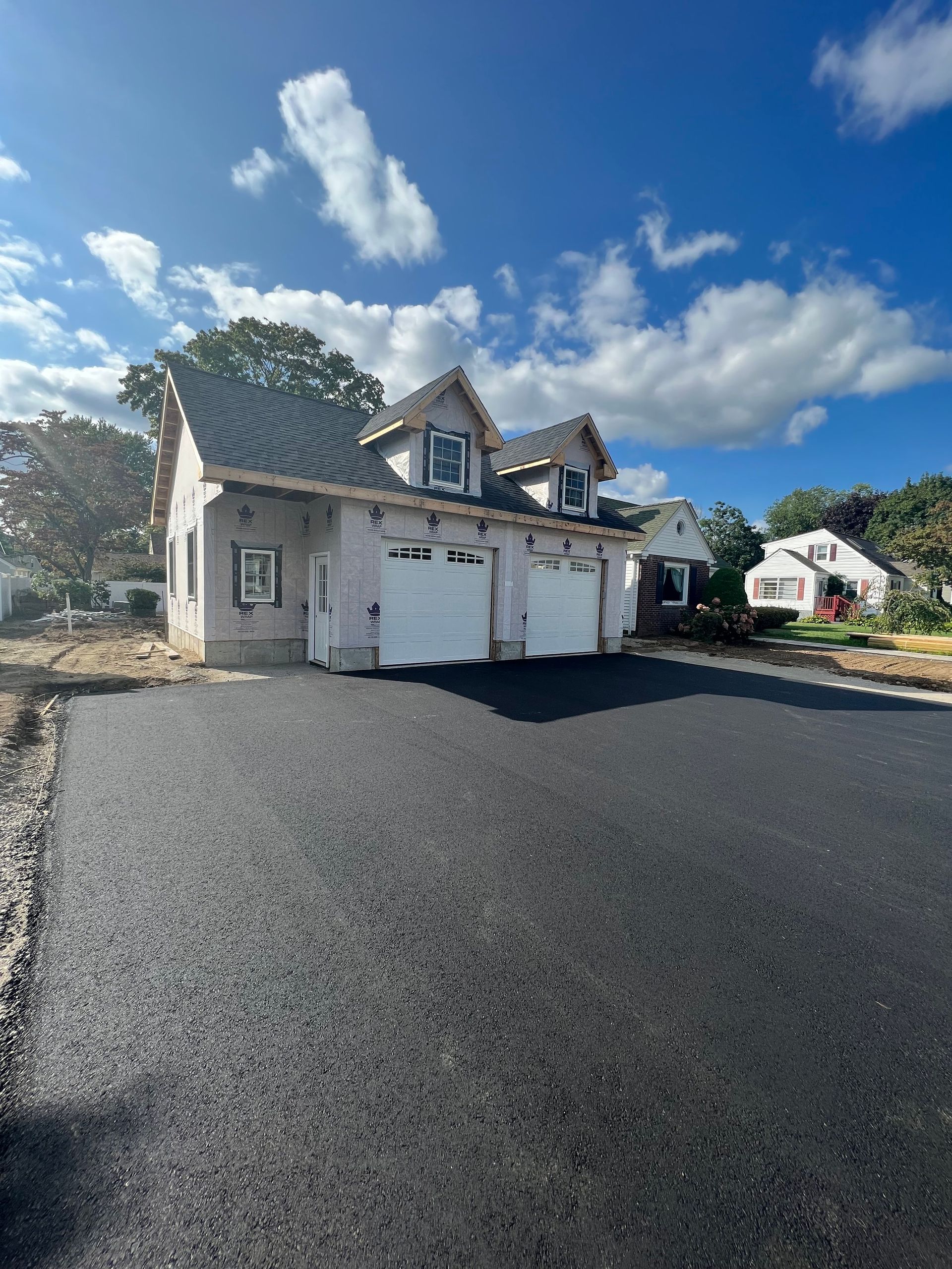 New construction, light gray building with two garage doors and asphalt driveway, under a cloudy sky.