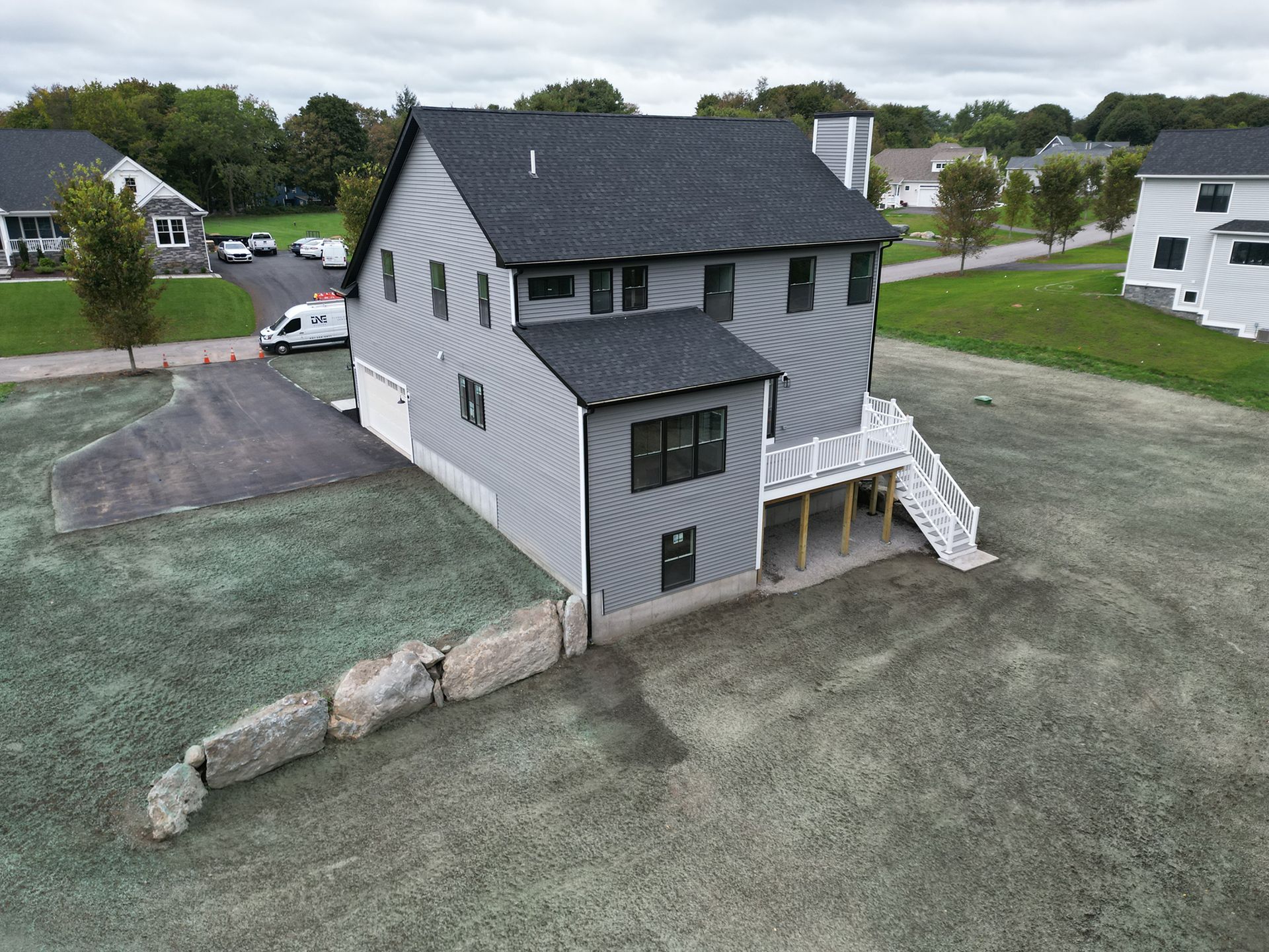 Gray house with dark roof and white deck, situated on a grassy lot.