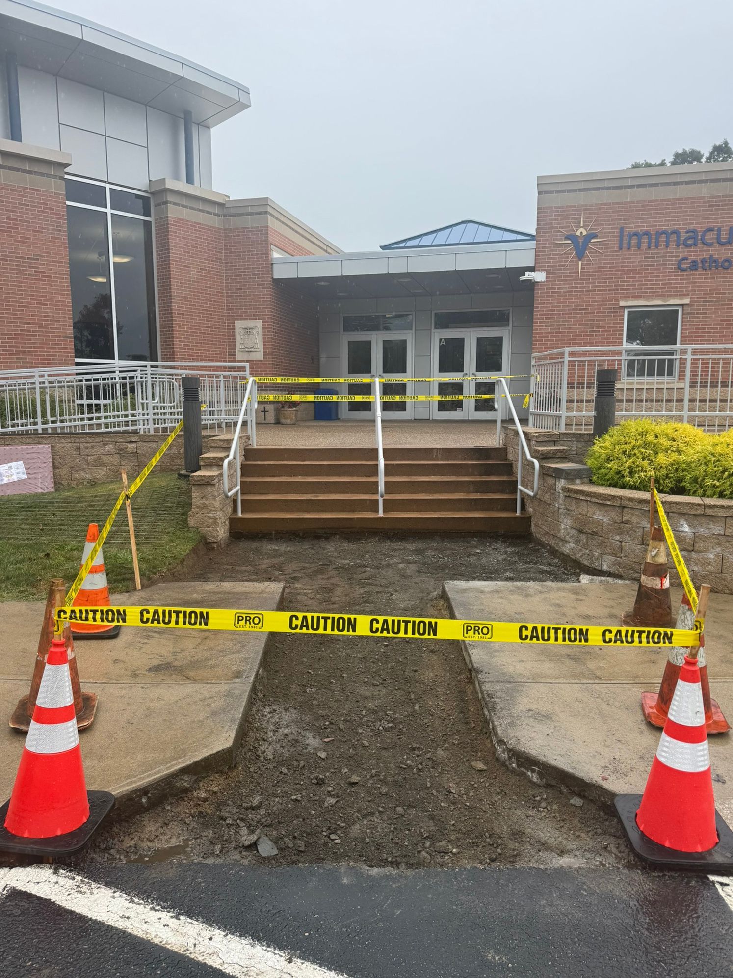 Entrance to Immaculate Conception Church blocked by construction. Gravel path, stairs, caution tape, orange cones.