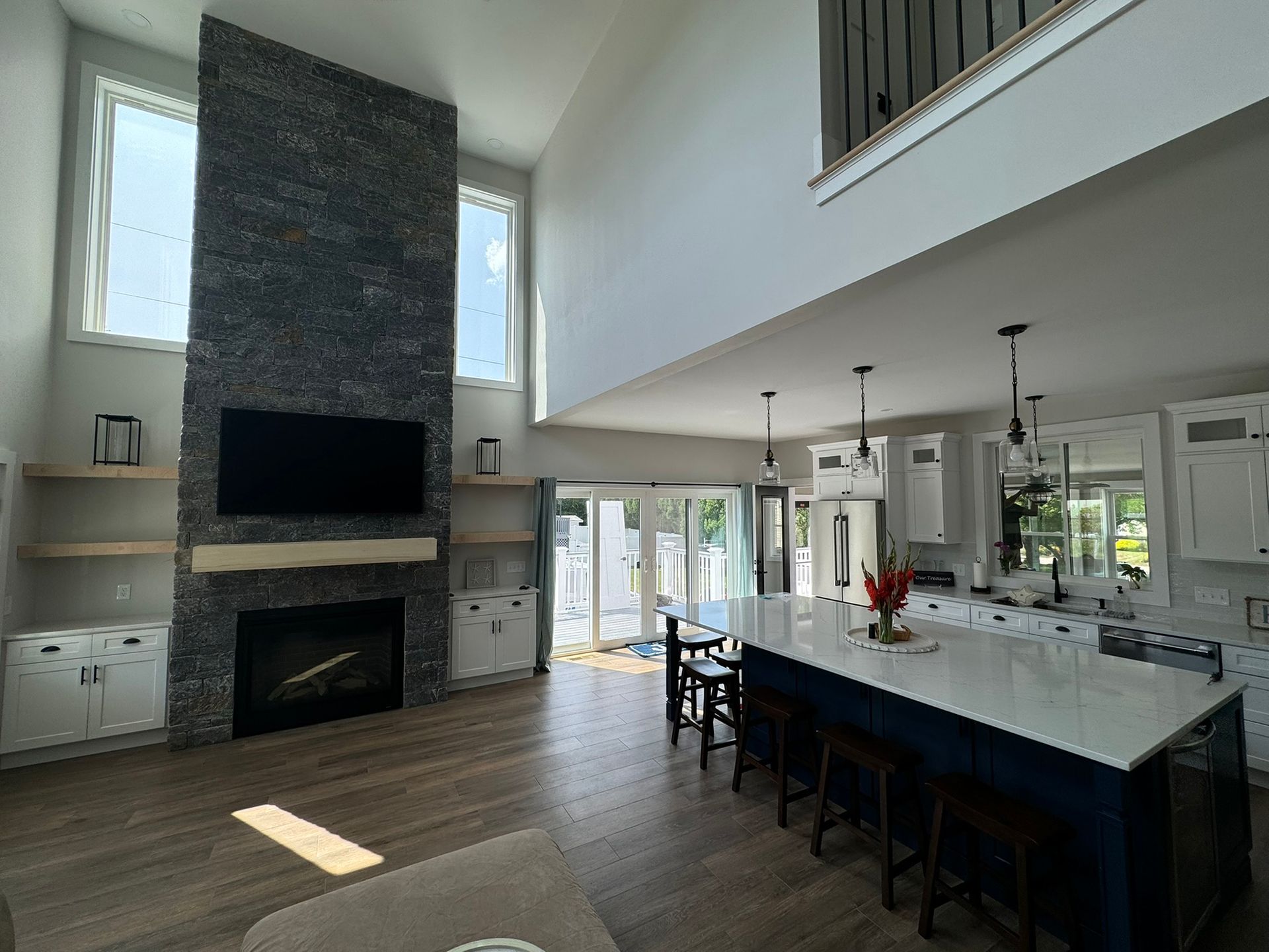 Open-concept living space with a stone fireplace, kitchen island, and high ceilings.