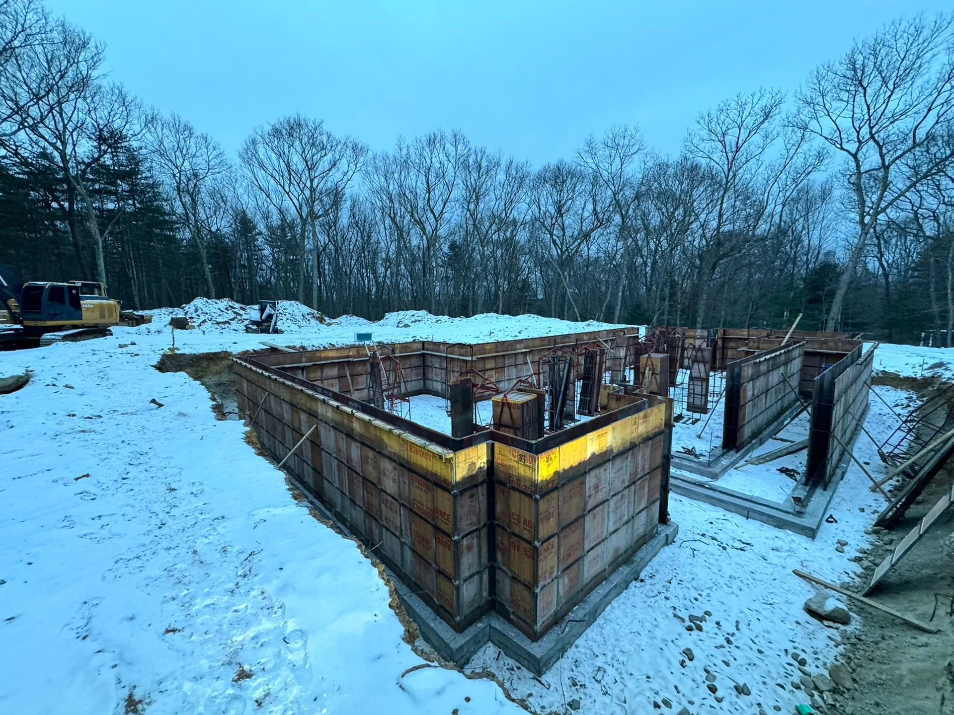Foundation forms for a building under construction, set in snow-covered ground with trees in background.