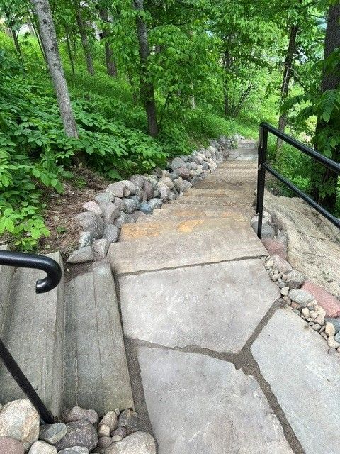 Steep stone walkway with black railings winding through a green wooded area