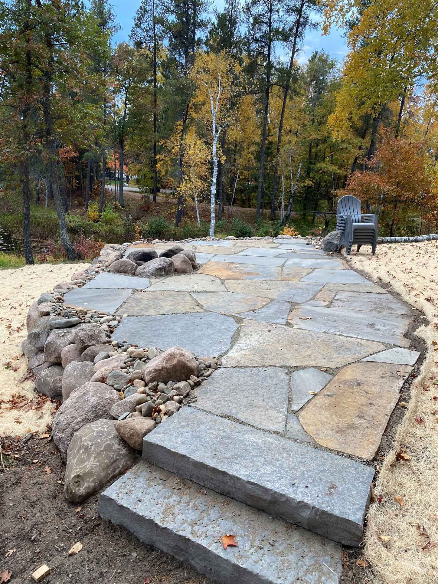 Stone path with steps through a wooded park, bordered by rocks and autumn trees
