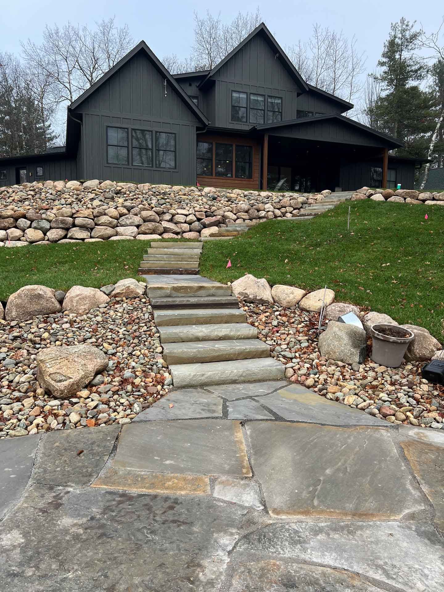 Stone steps leading to a dark gray house with a landscaped rock garden and green lawn
