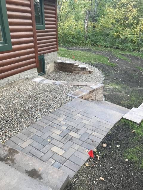 Brick pathway and steps leading to a cabin with gravel and a retaining wall.