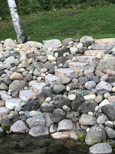 Stone steps leading up a rock-covered embankment to a grassy area with a tree.