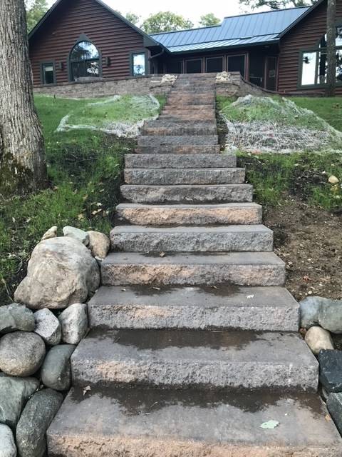 Stone steps leading up to a wooden cabin-style house on a grassy hill.