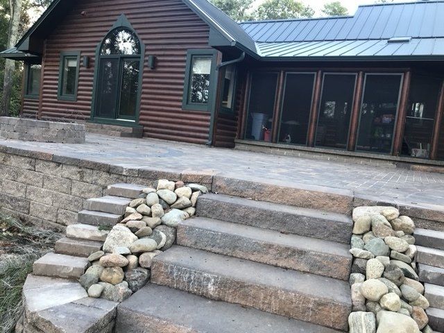 A rustic cabin with stone stairs and a patio, surrounded by rock walls.