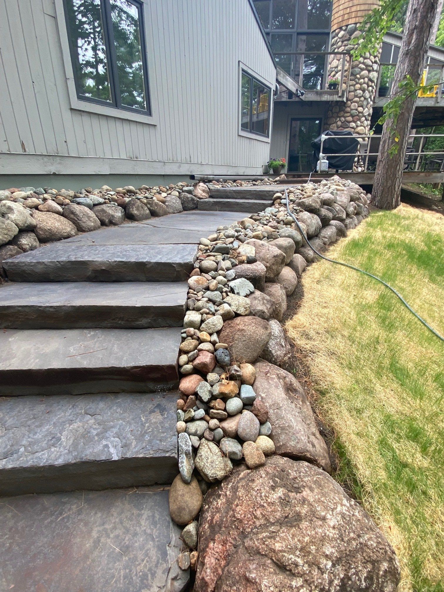 Stone steps leading to a house with a rock retaining wall, bordered by grass.