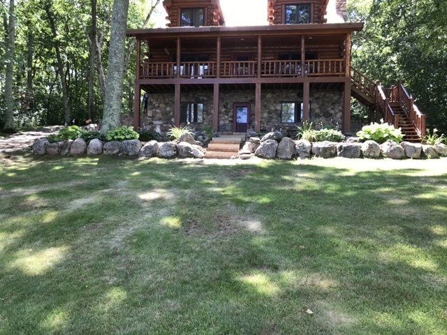 Log cabin with stone foundation, two levels of balconies, and large lawn.