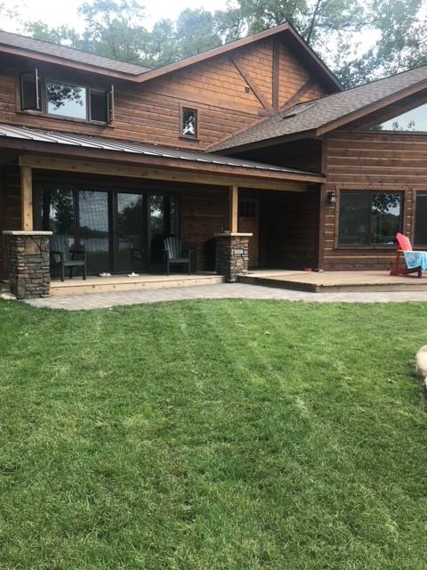 Wood-sided house with porch, stone pillars, and lush green lawn.