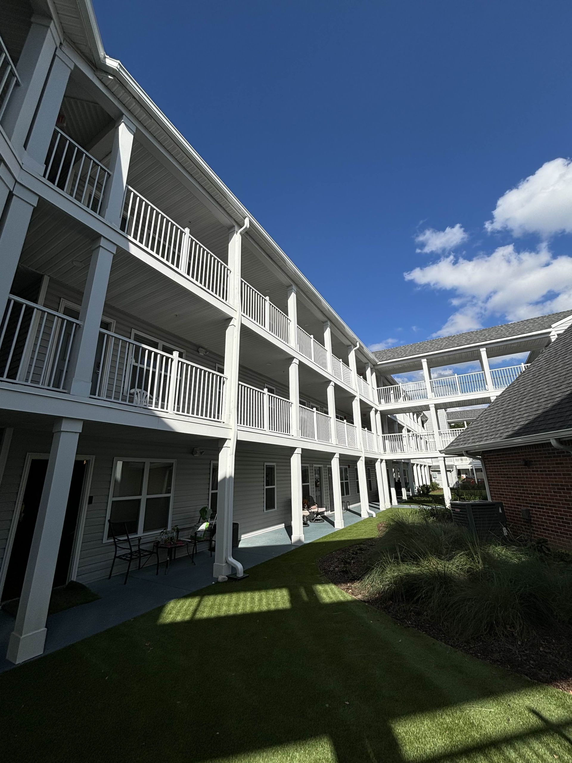 White apartment building with balconies and green lawn under a bright blue sky