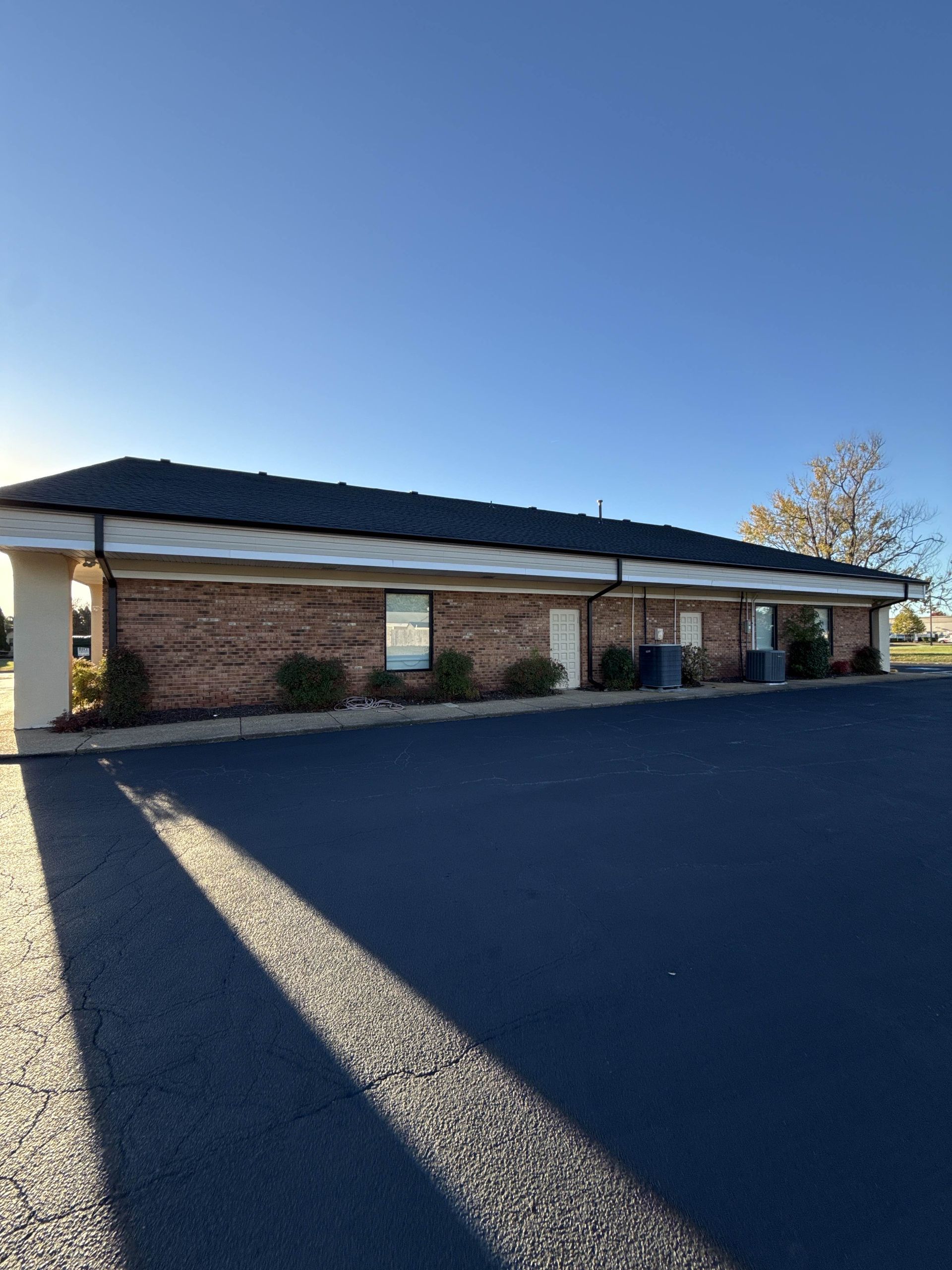 Single-story brick building with a dark roof beside a paved parking lot under a clear blue sky