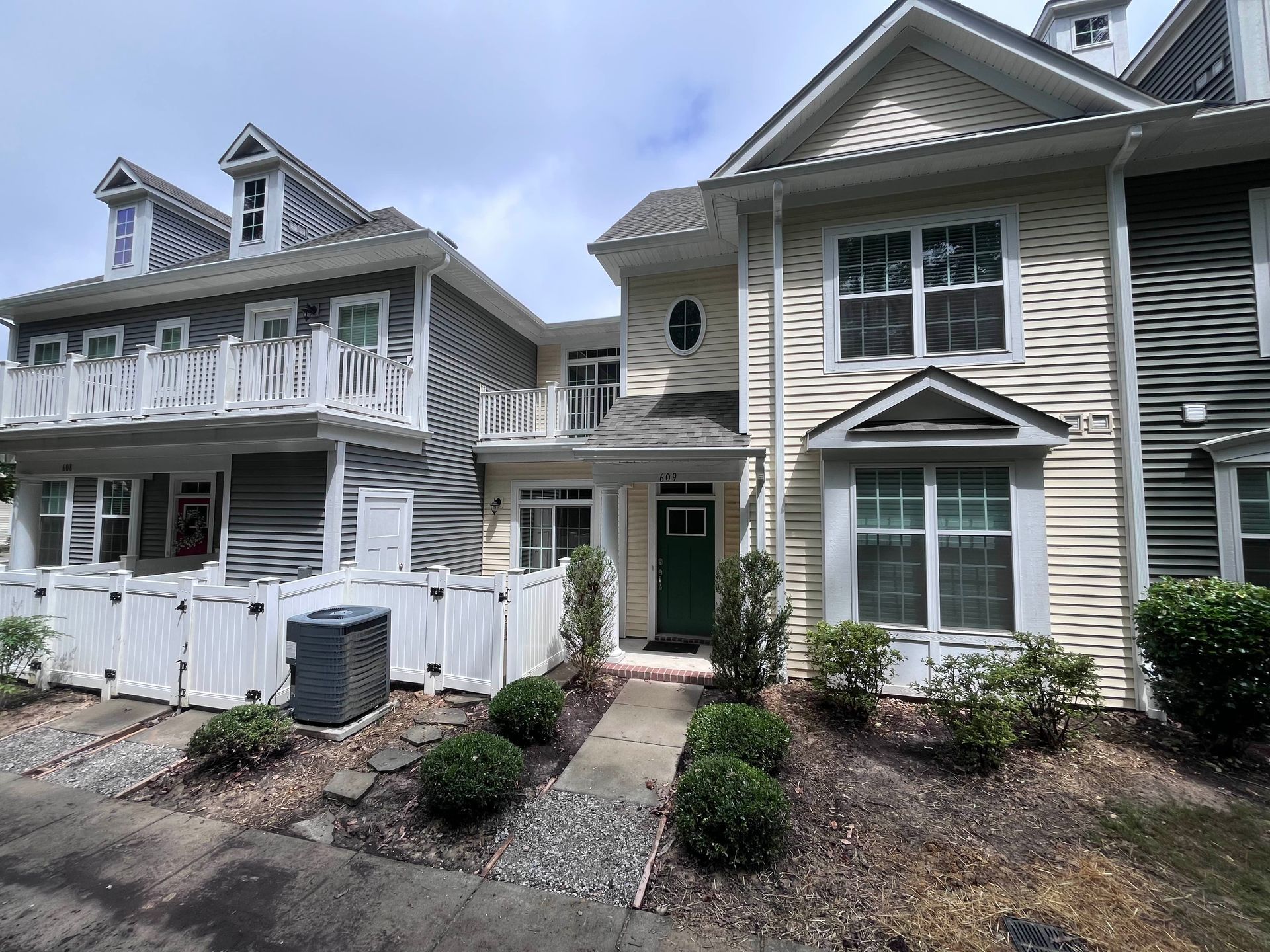 Row of gray townhouses with white trim, porches, green doors, and a small front path and shrubs
